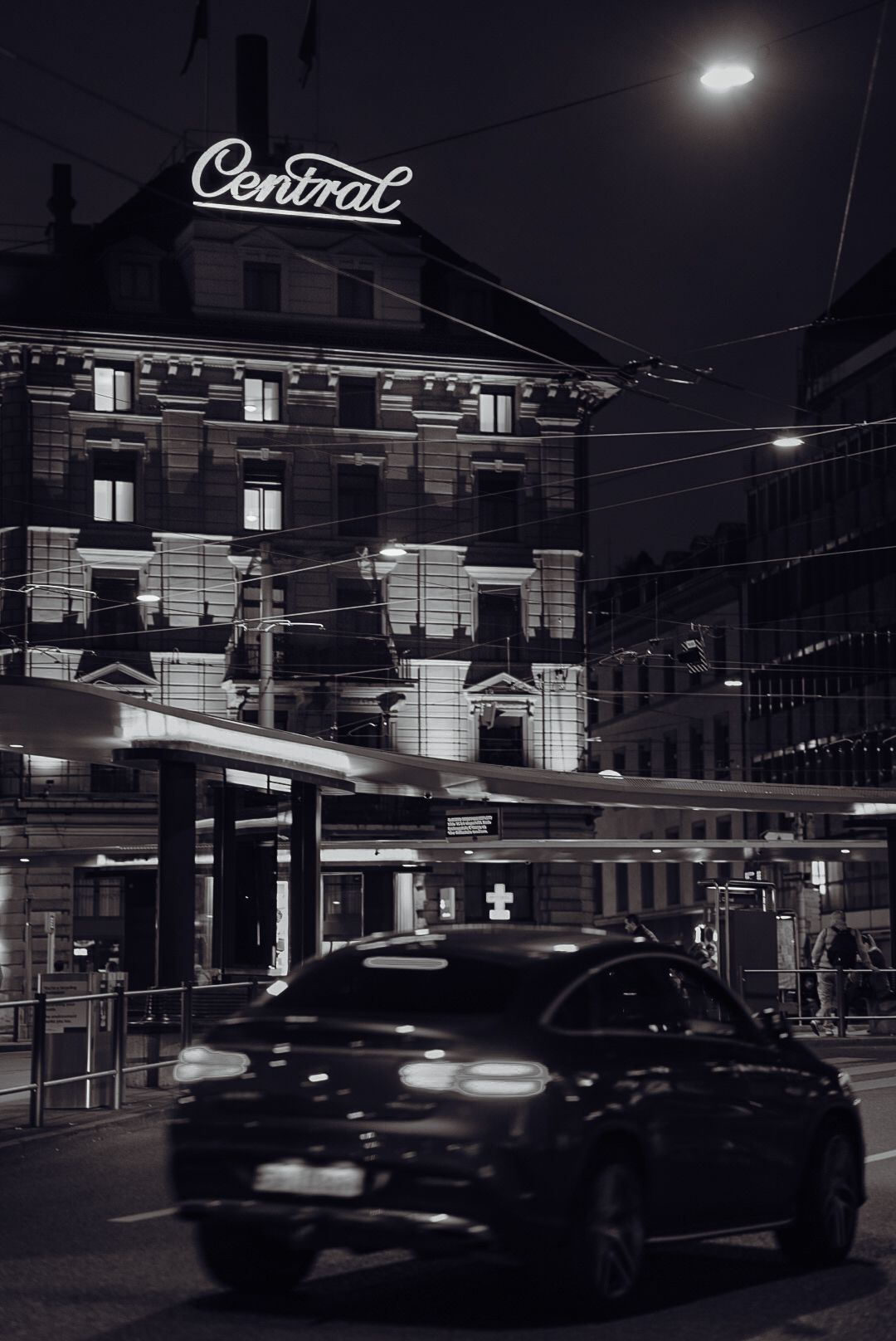 Night scene of an illuminated Central building with vintage signage and a car passing by.