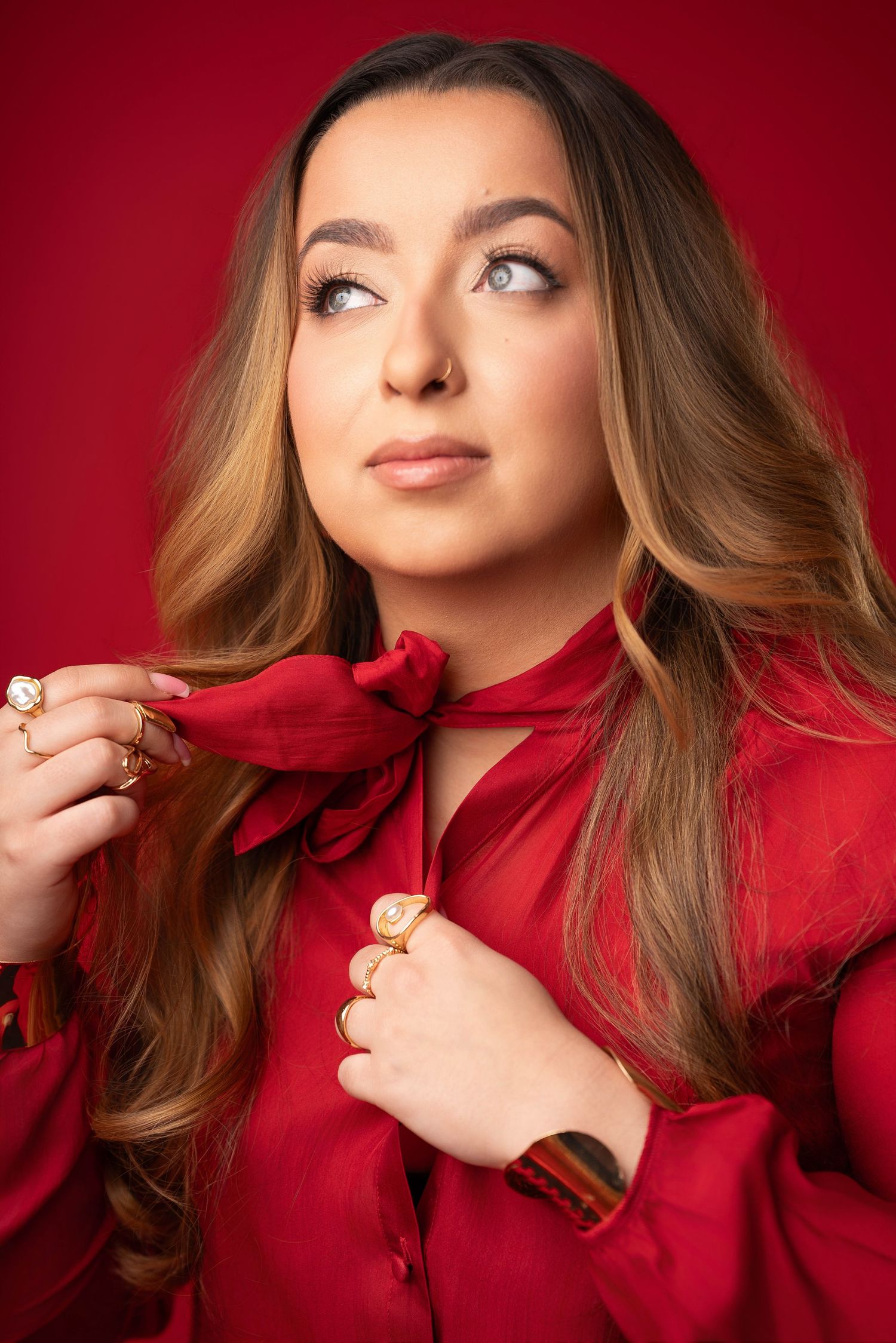 Fashion portrait against red backdrop showing person in vibrant red blouse with wavy brown hair in dynamic poses.