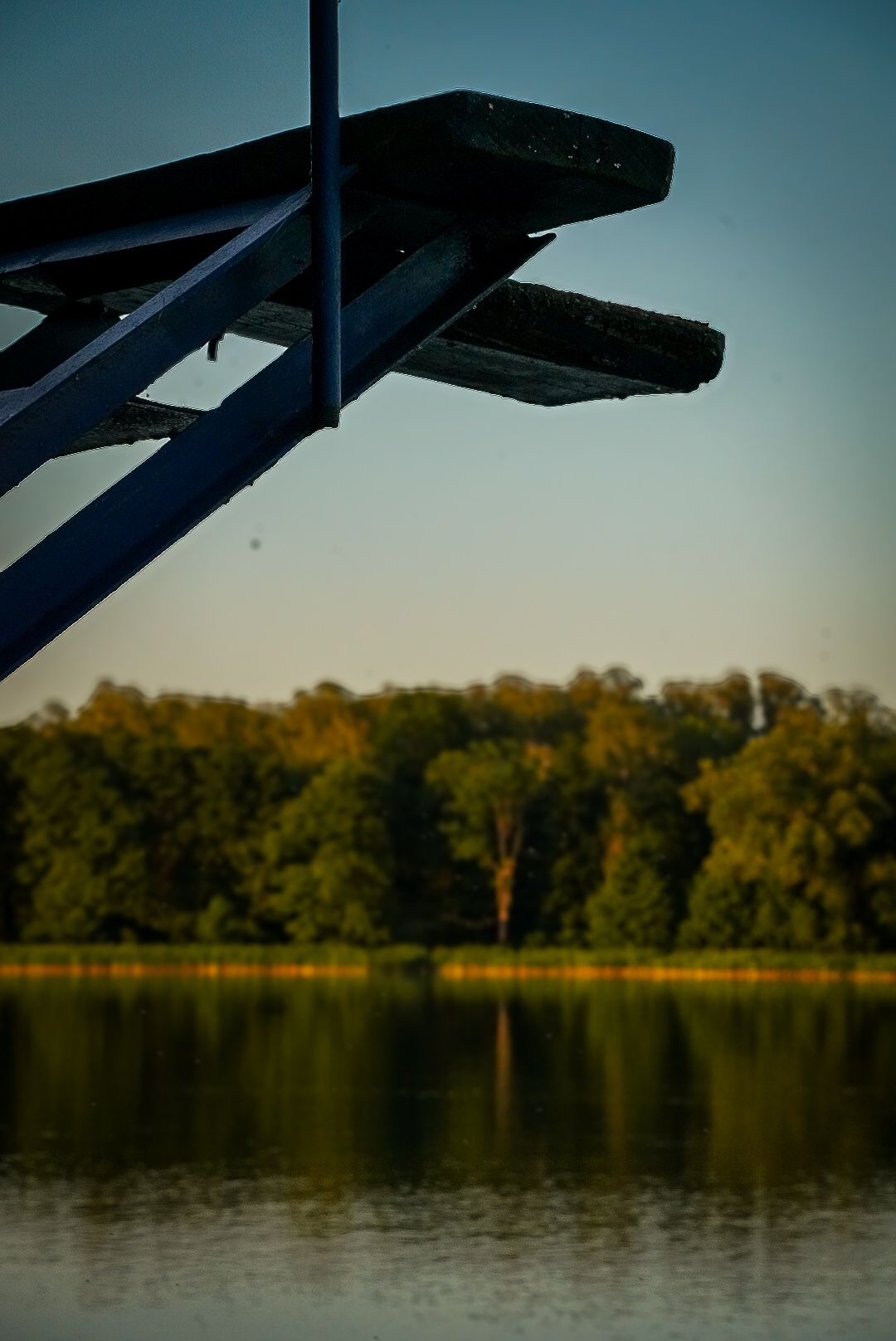 Silhouette of a diving board against a lakeside sunset.