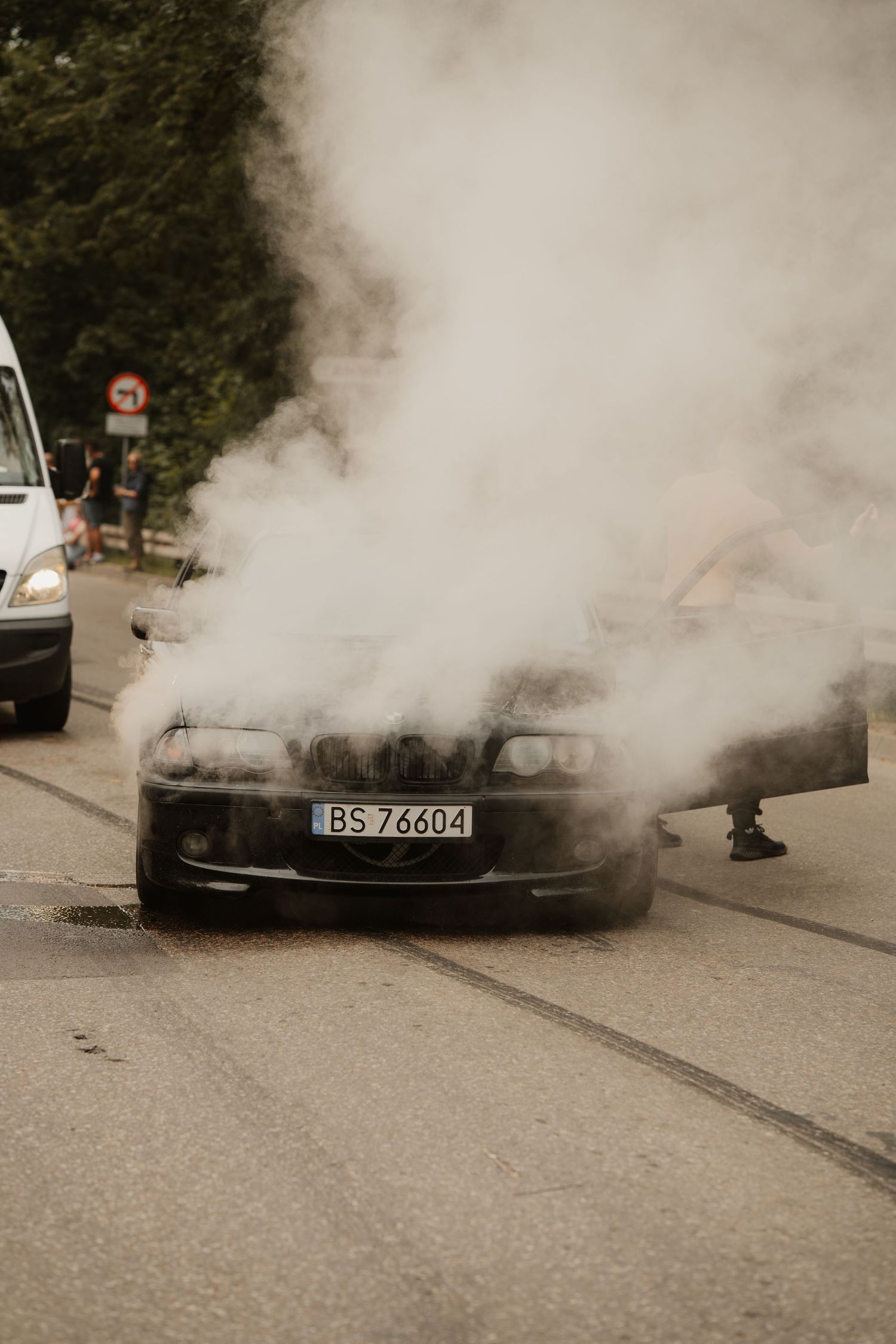Car engine smoking heavily and producing thick white smoke on a city street from suspected mechanical failure.