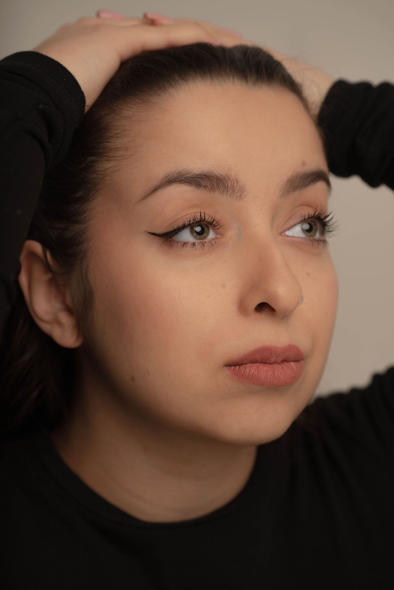 Beauty portrait with clean makeup, defined brows and black top against neutral background.