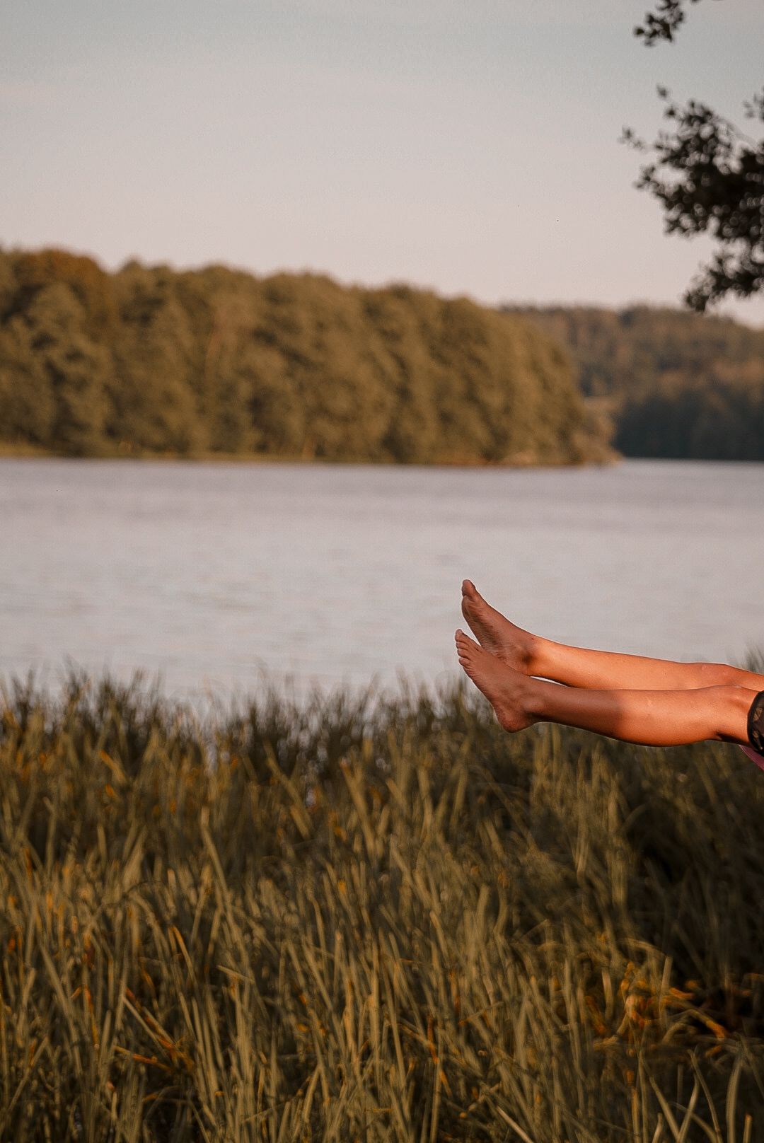 Bare feet relaxing by a serene lake surrounded by trees at golden hour.