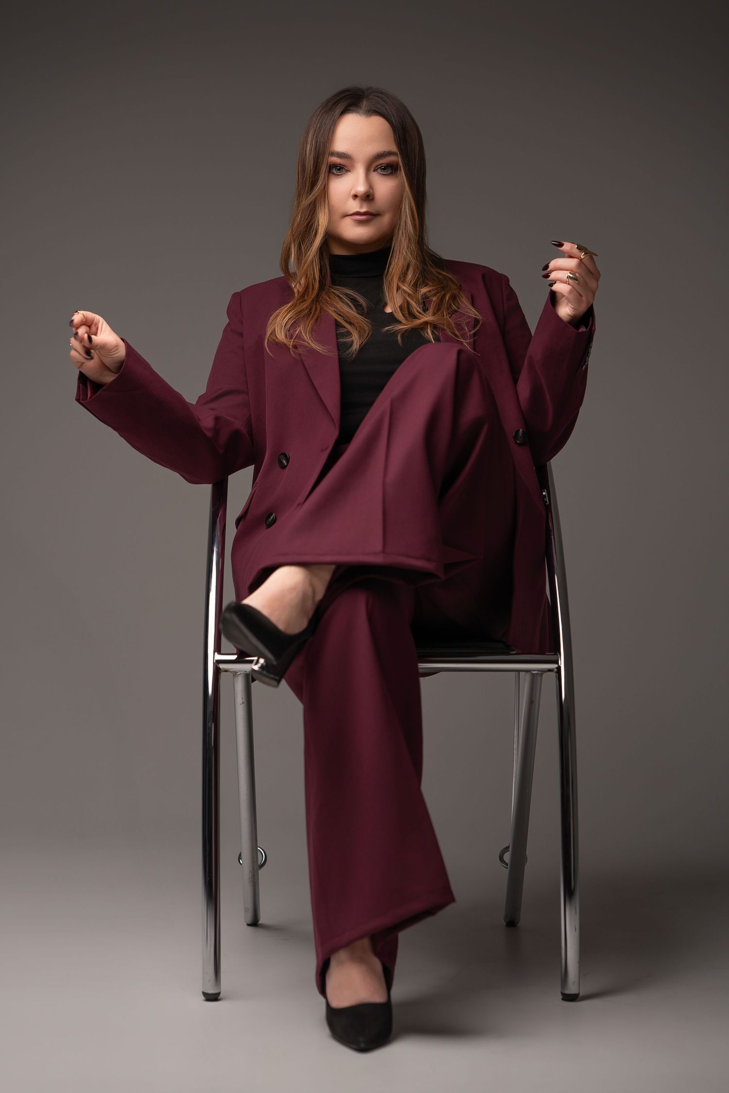A fashion photo series showing someone in a burgundy oversized sweater dress posing on a modern chair against gray backdrop.