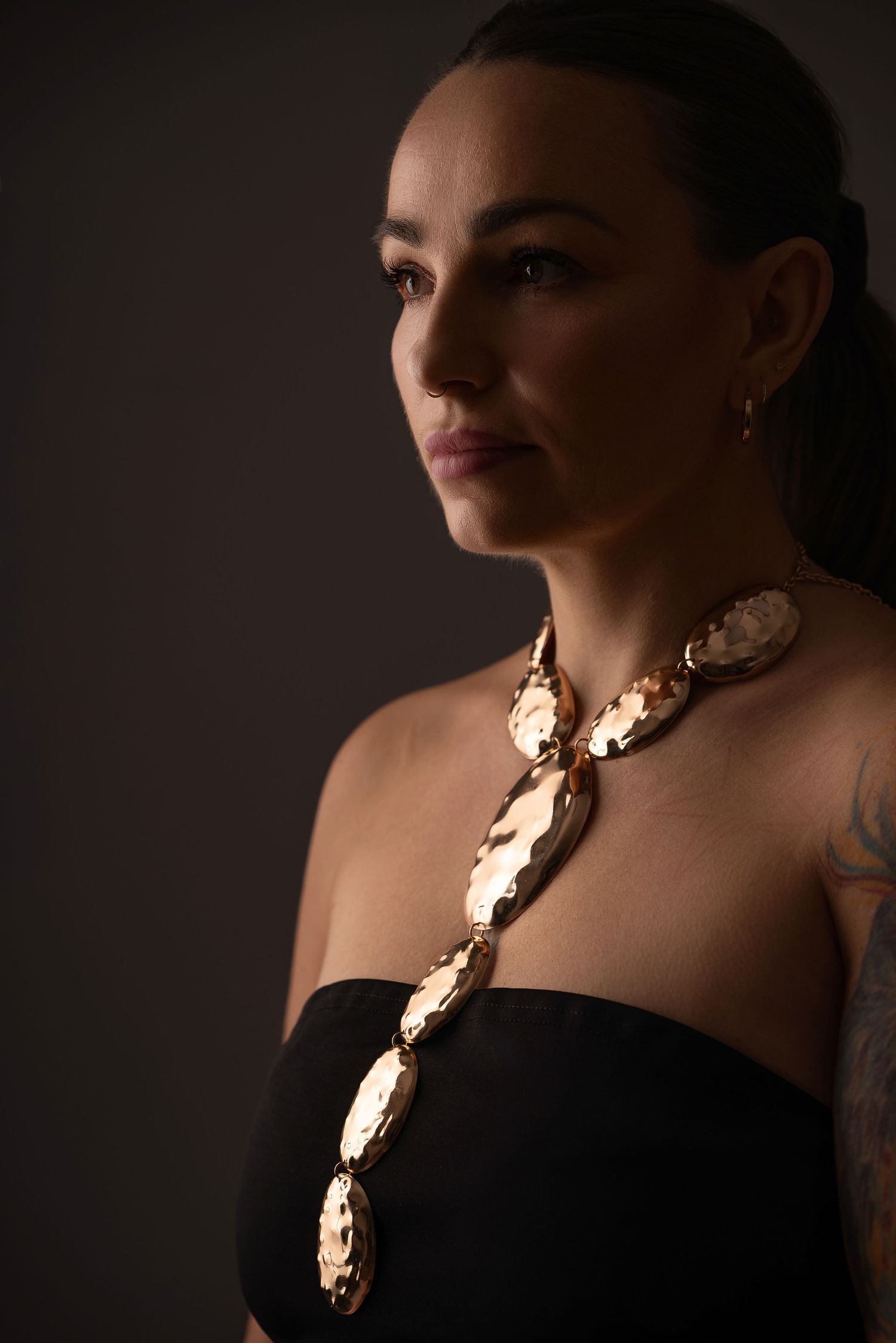 Dramatic profile portrait series showing gold statement necklace against black dress in moody lighting.