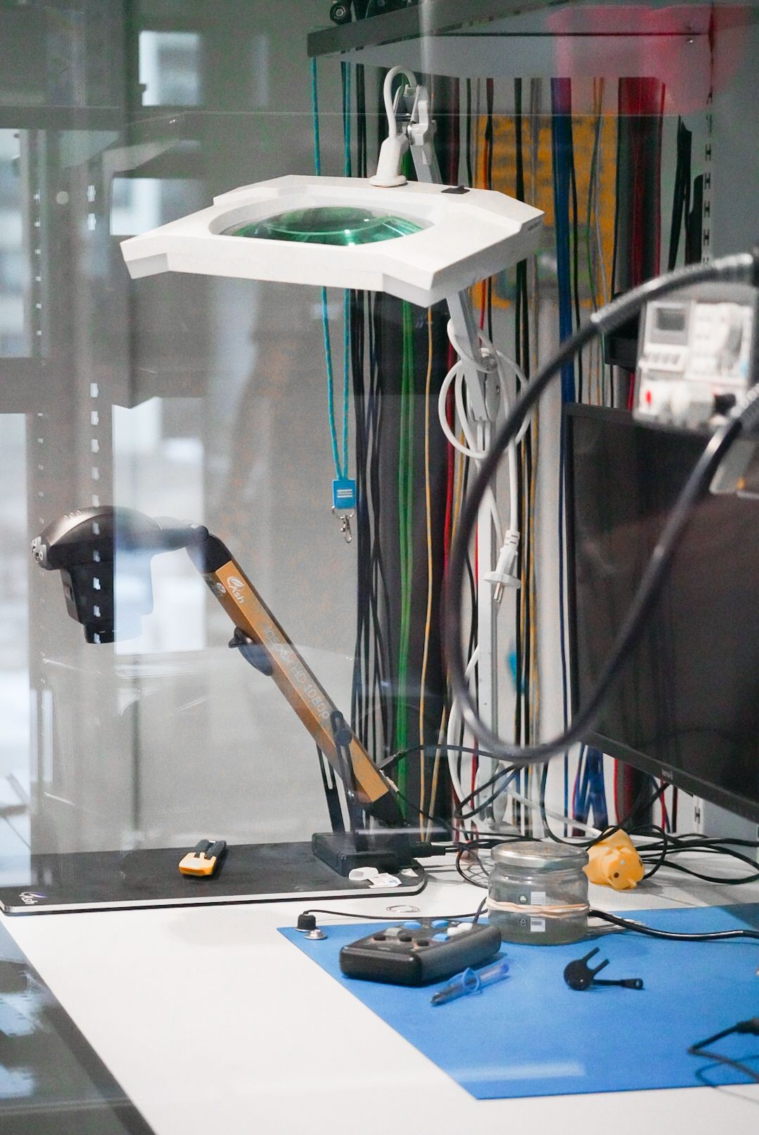 Electronics workbench with magnifying glass and various tools on blue work surface.