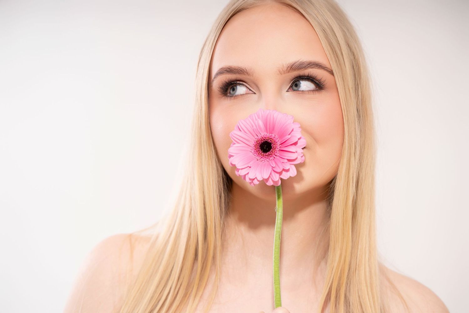 A series of three photos shows someone playfully posing with a pink gerbera daisy flower against a white background.