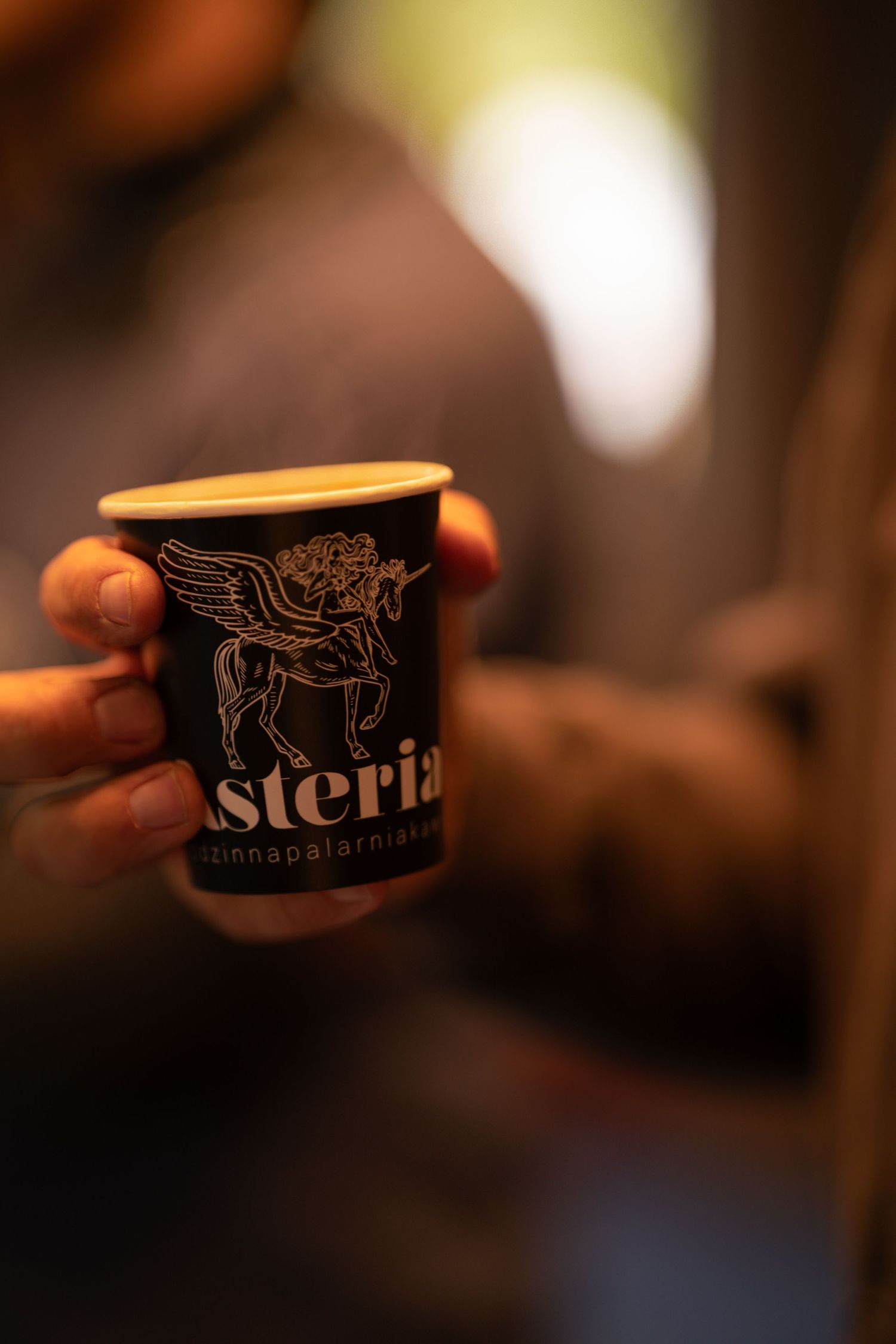 Sesja produktowa, kubek kawy z logo, ciepłe odcienie, mocny bokeh.