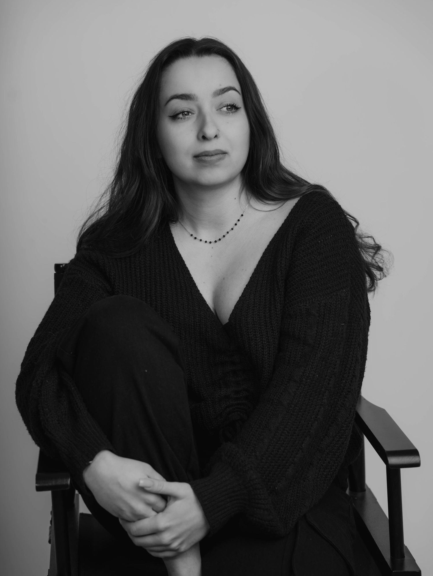 Artistic black and white portrait in black sweater seated in chair.