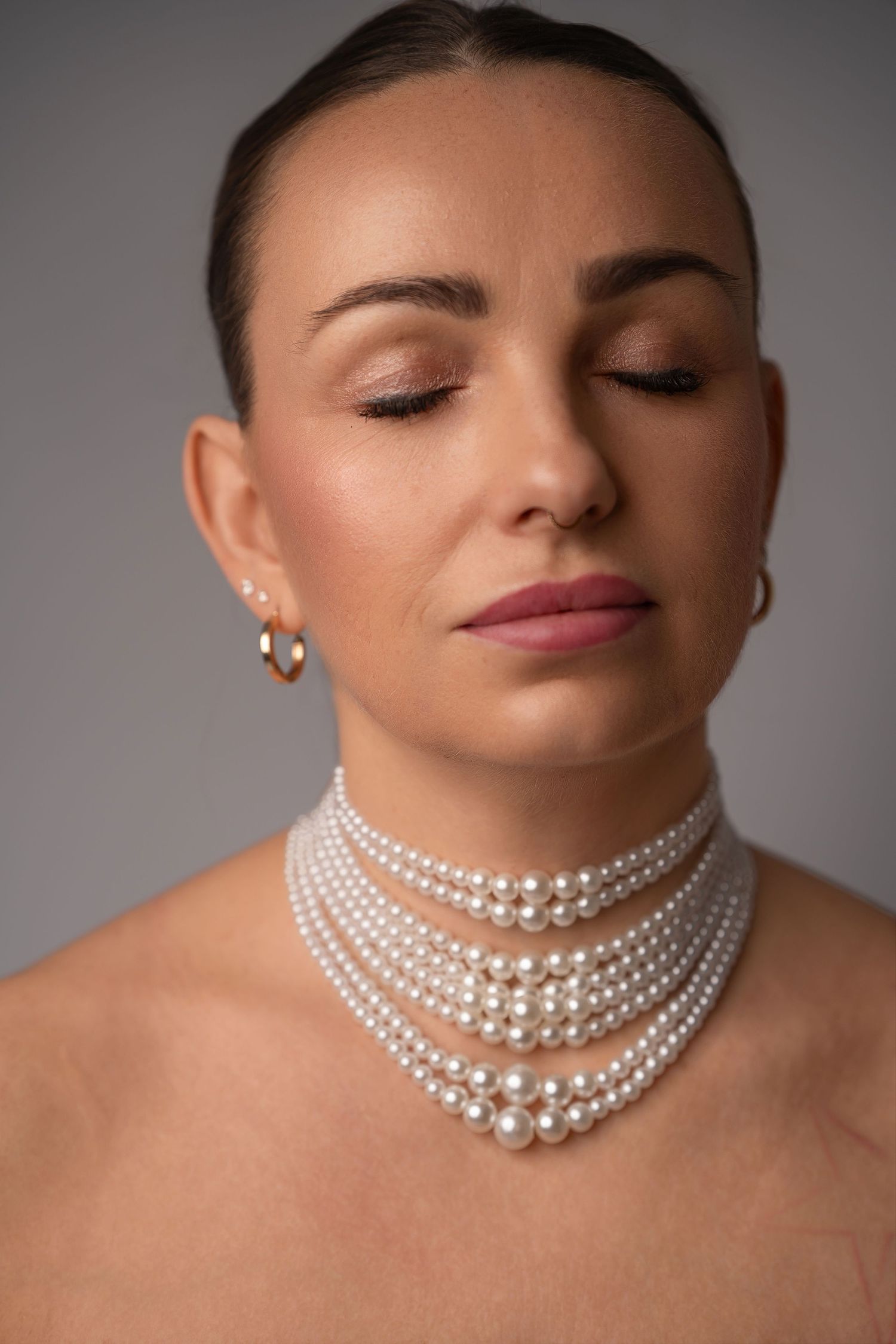 A series of fashion photos showing an elegant pearl necklace styled in different ways against a gray backdrop.