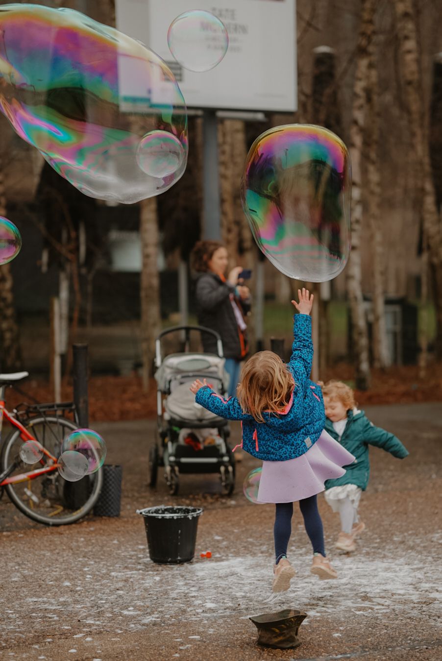 Large iridescent soap bubbles float as children play outdoors near a parked bicycle.