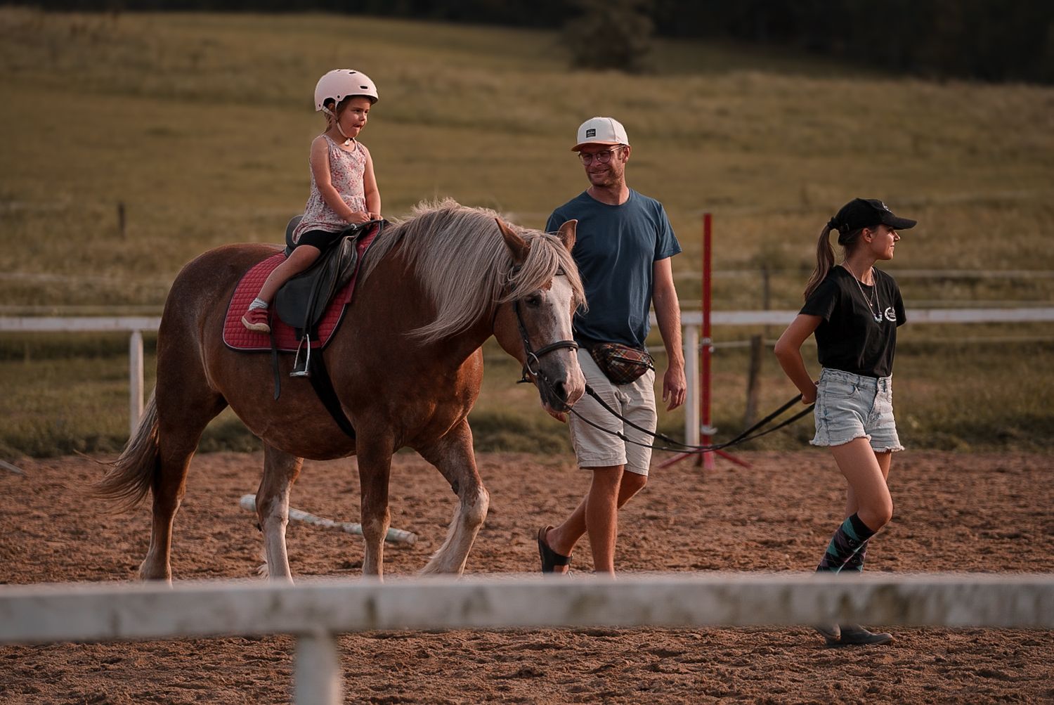 Horse riding lesson taking place in an outdoor arena at sunset.