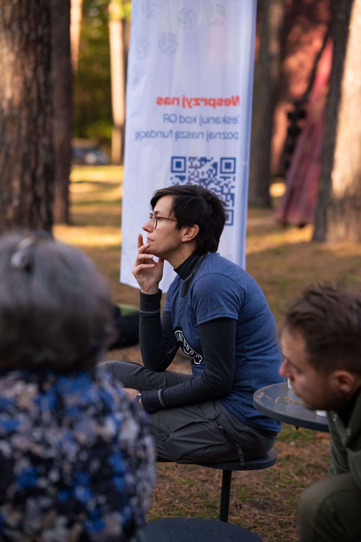 Someone in a blue shirt sitting thoughtfully outdoors near a QR code banner.