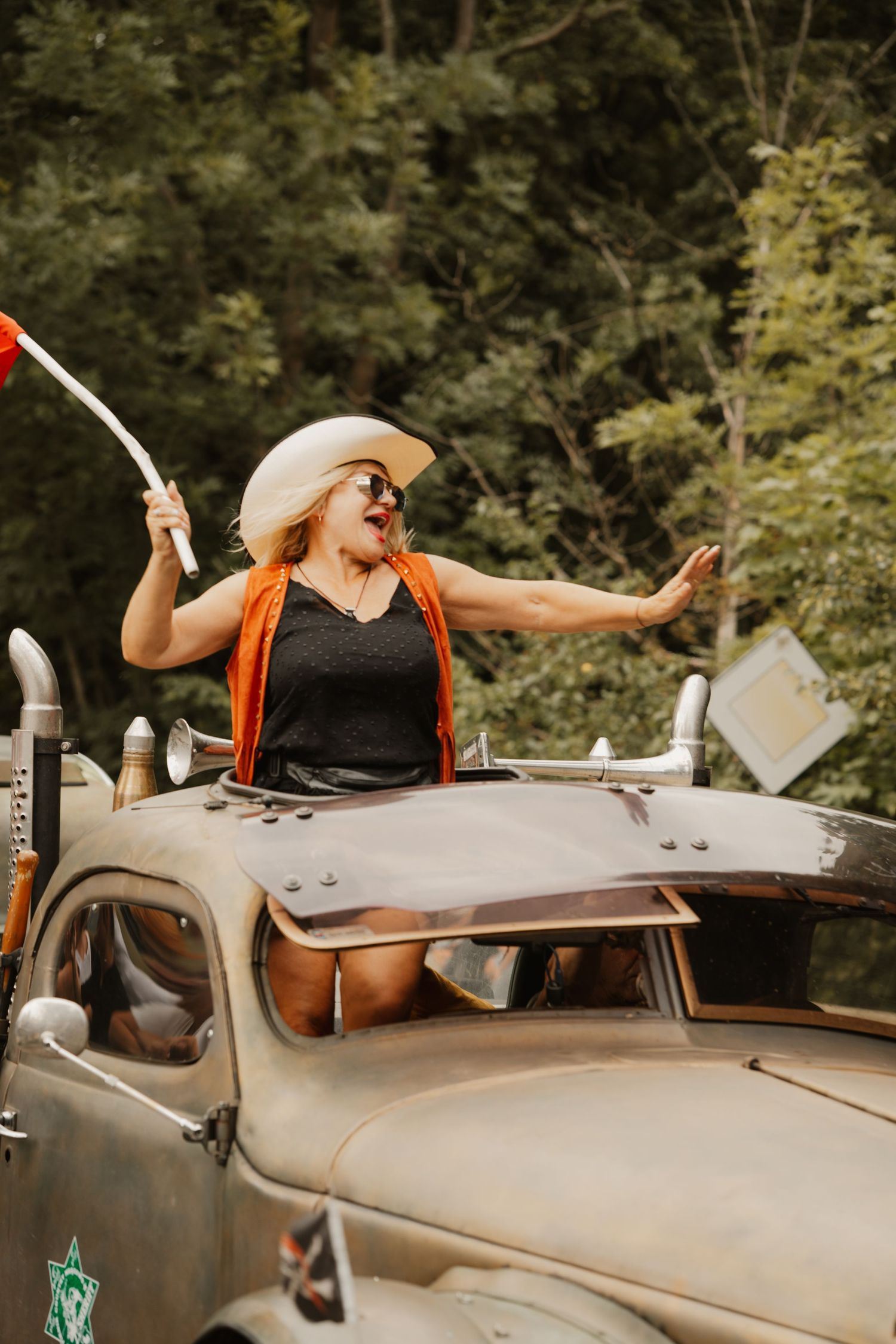 A vintage truck features someone in a cowboy hat and orange suspenders posing energetically through the sunroof.
