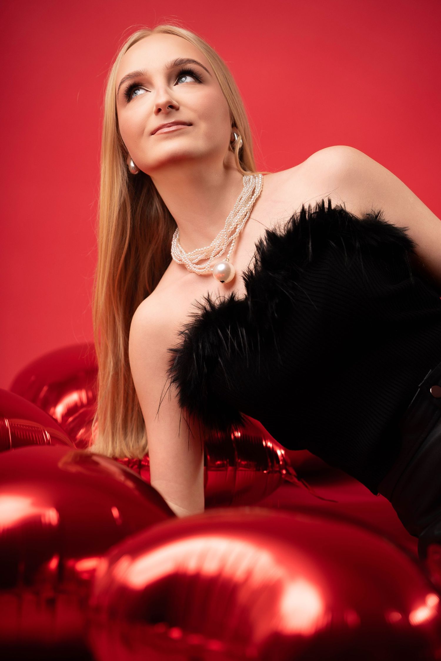 Glamorous fashion portrait against red backdrop with black feather accessory and dramatic lighting effects.
