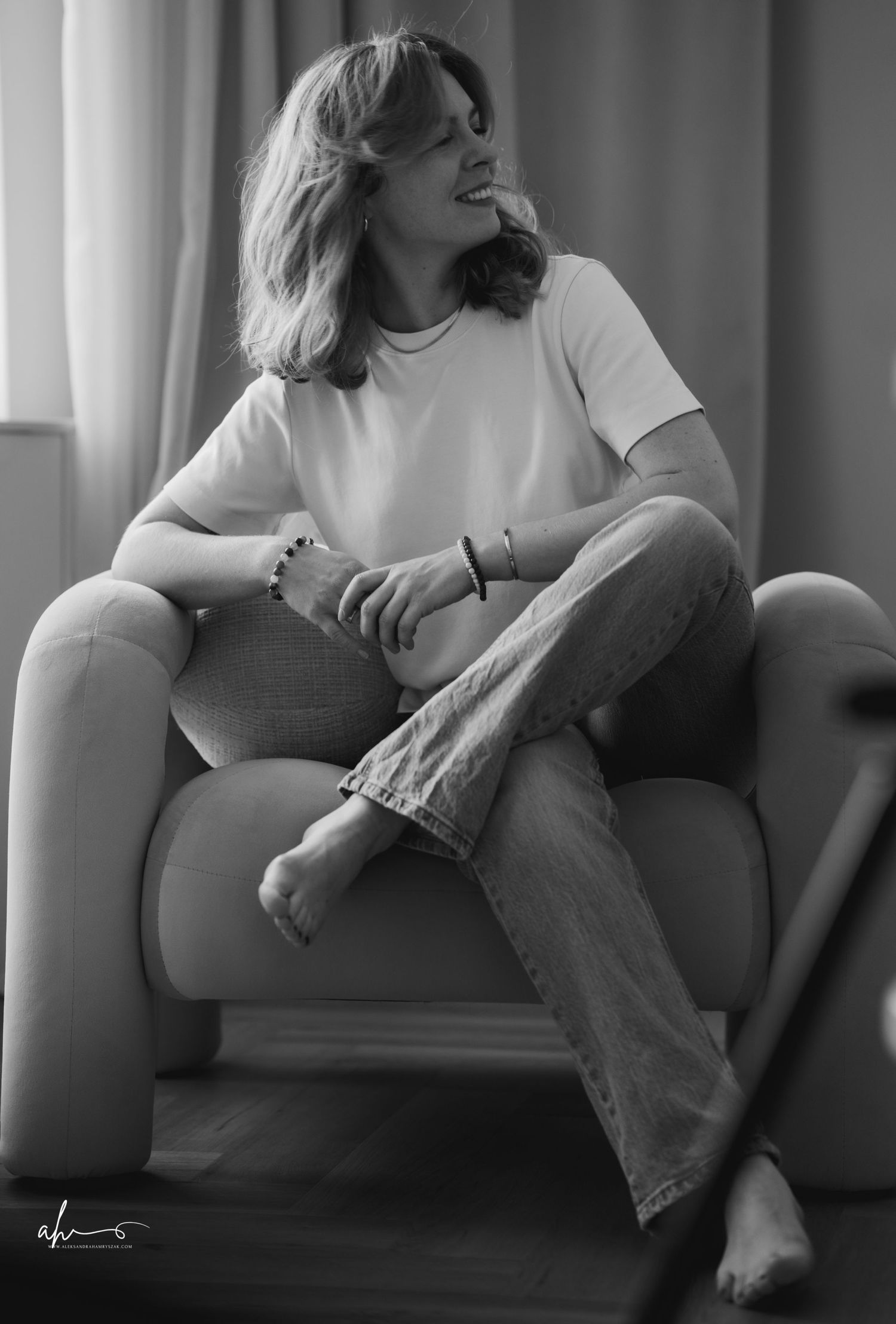 A black and white portrait of someone relaxed in a comfortable armchair wearing jeans and a casual white t-shirt.