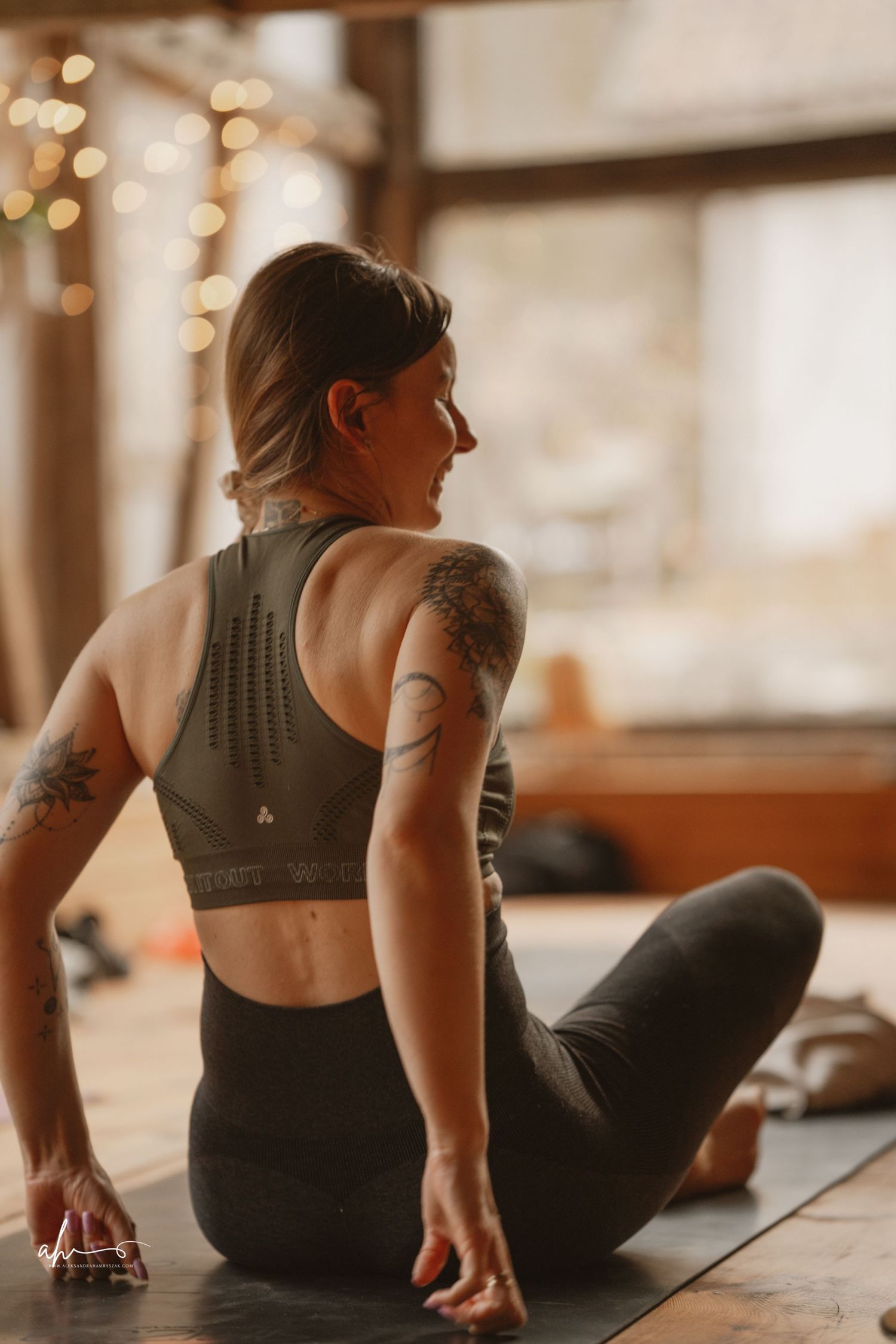 Athletic person in workout attire sitting on a yoga mat with warm lighting and bokeh effects in the background.