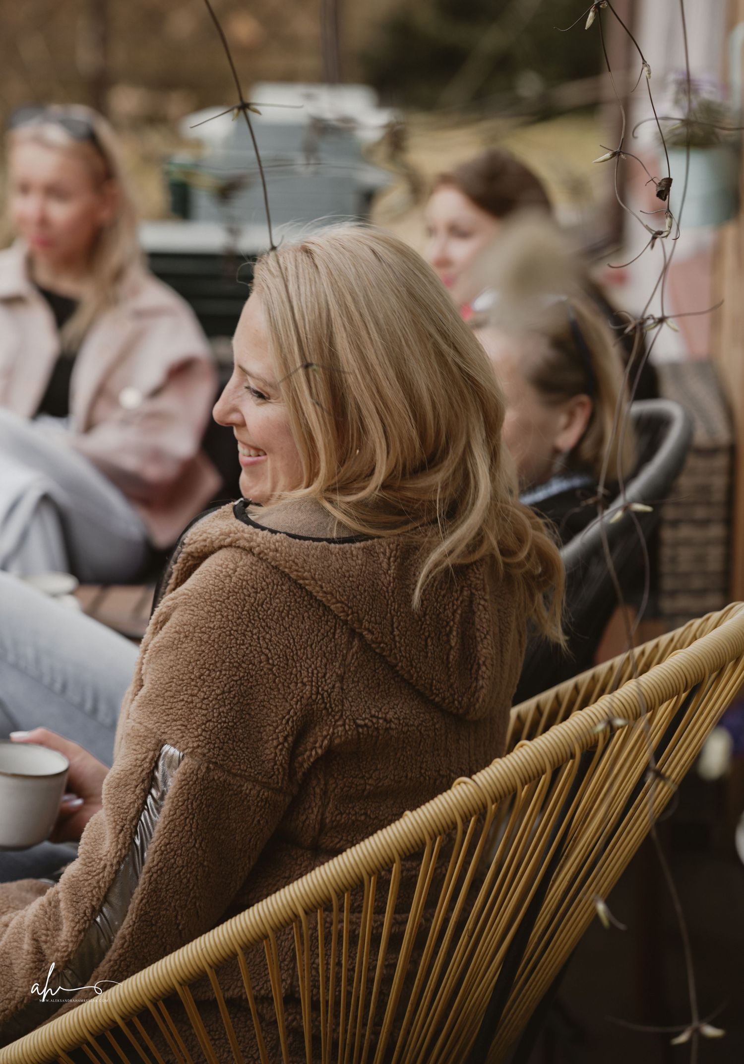 People relaxing outdoors on wicker patio furniture with a cozy brown teddy coat in focus.