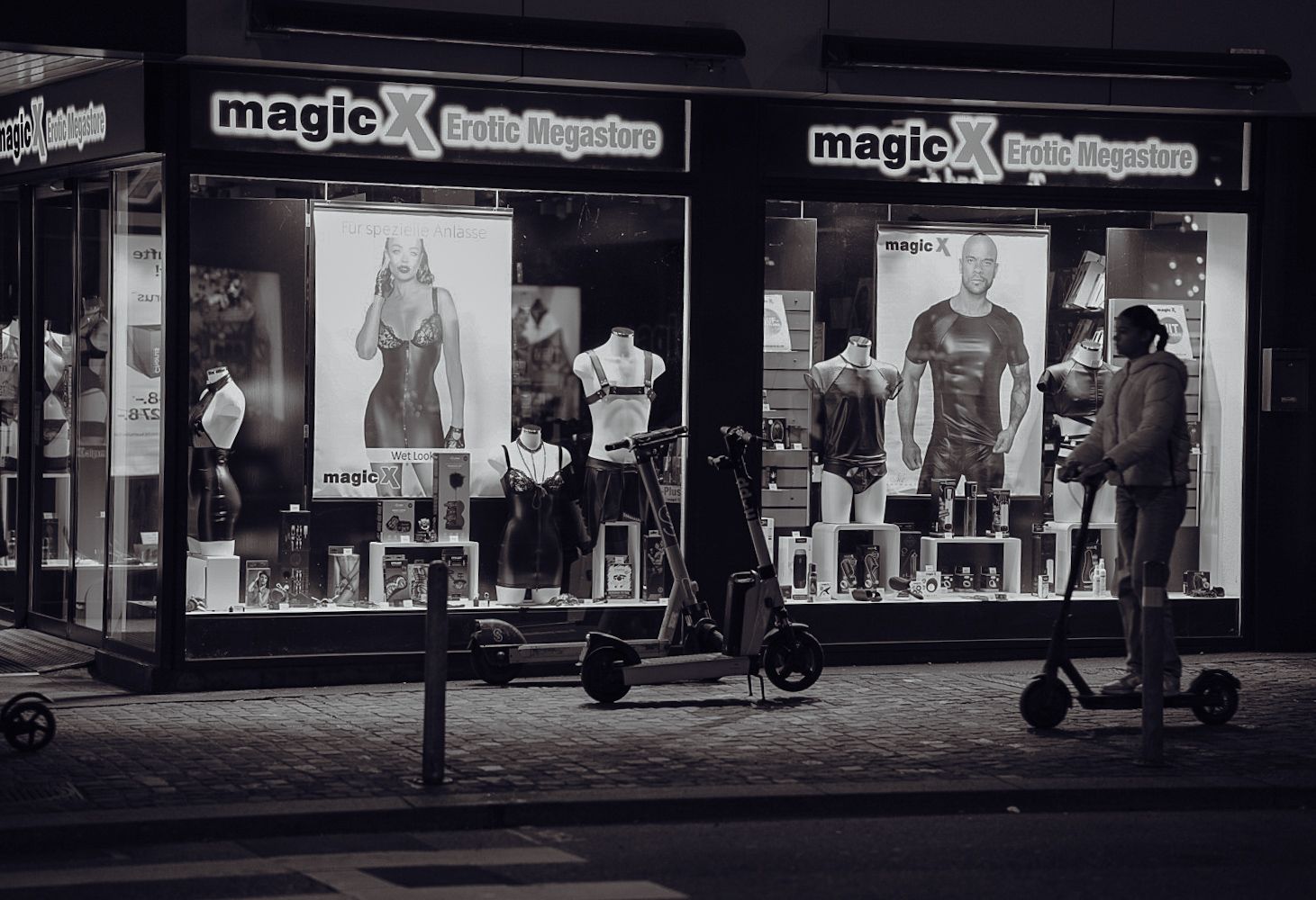 Black and white storefront of a clothing shop with window displays and electric scooters parked outside.