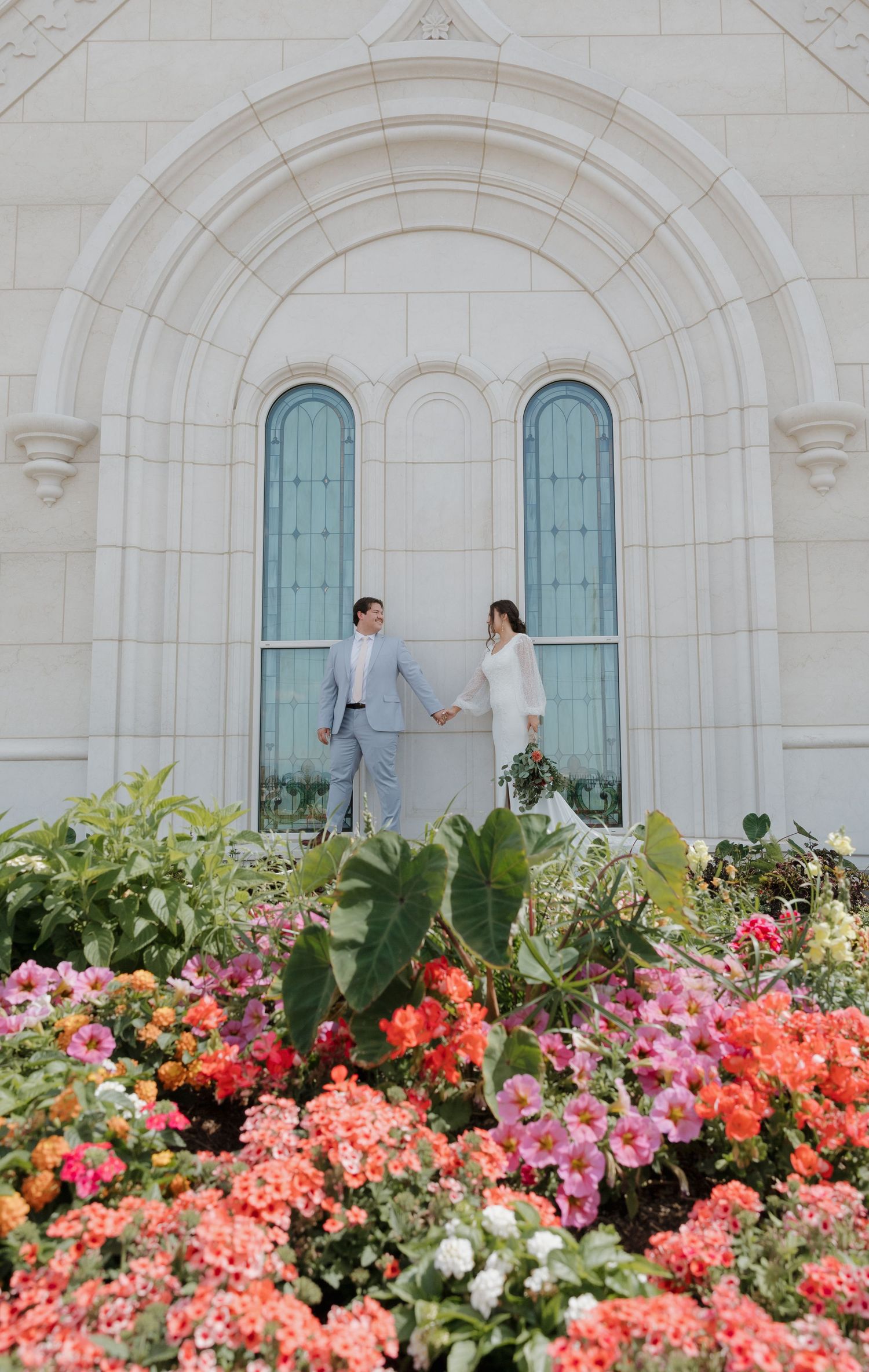 Wedding couple standing in front of a white stone building with colorful florals in Utah