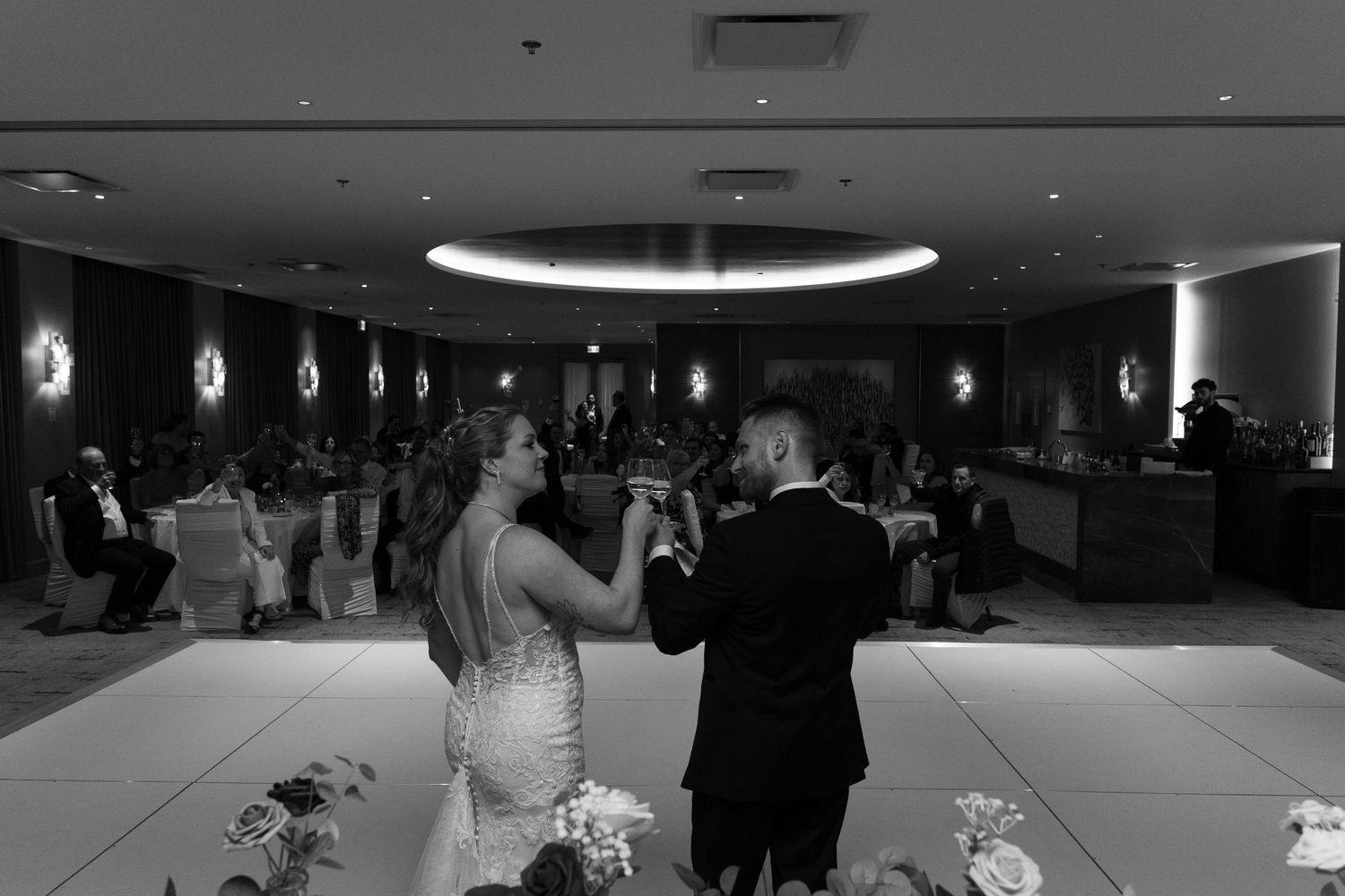 A couple shares their first dance at a wedding reception in a dimly lit ballroom with circular lighting overhead.