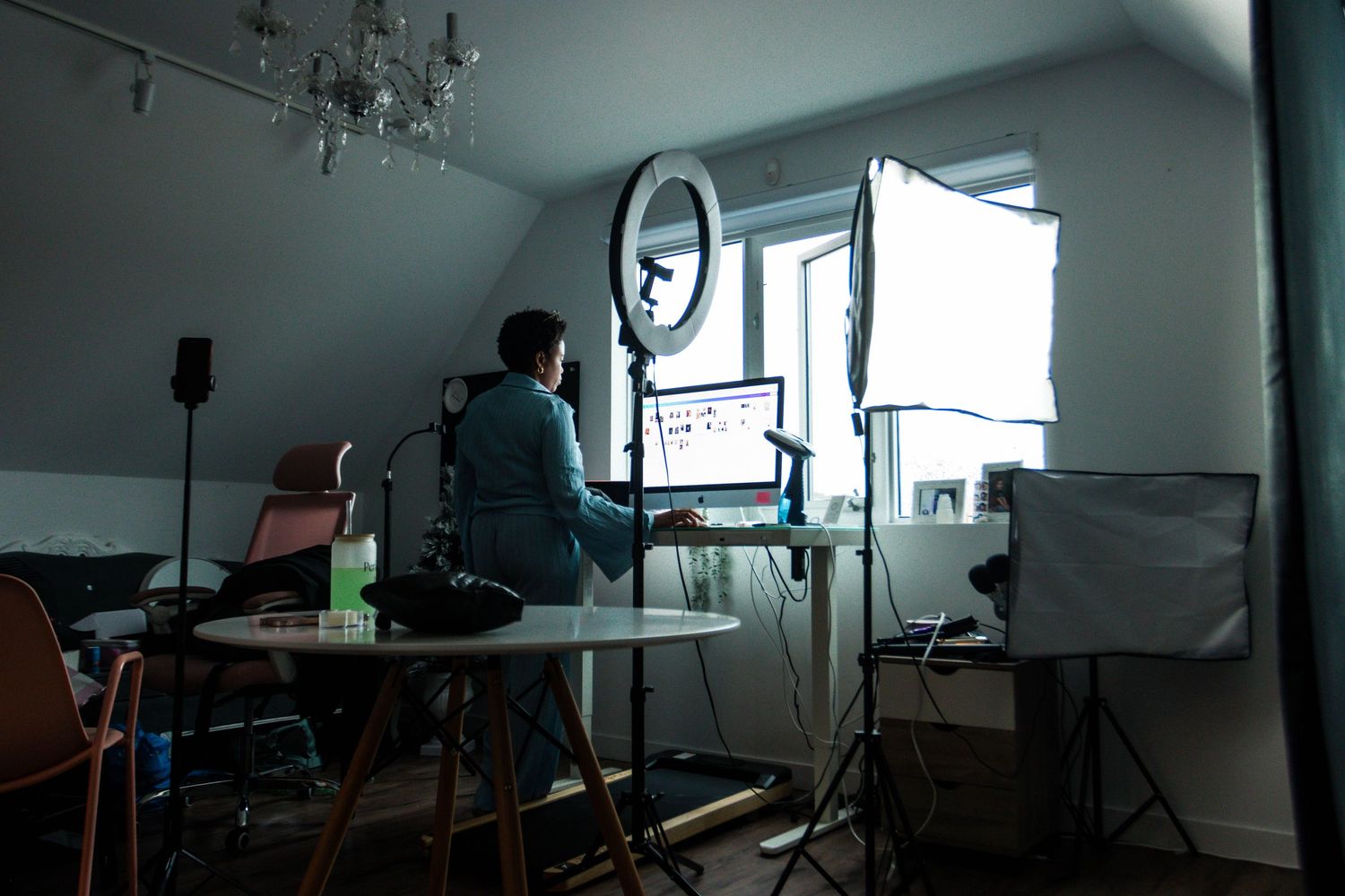 Silhouette of person working at desk with ring light and window in dark room.