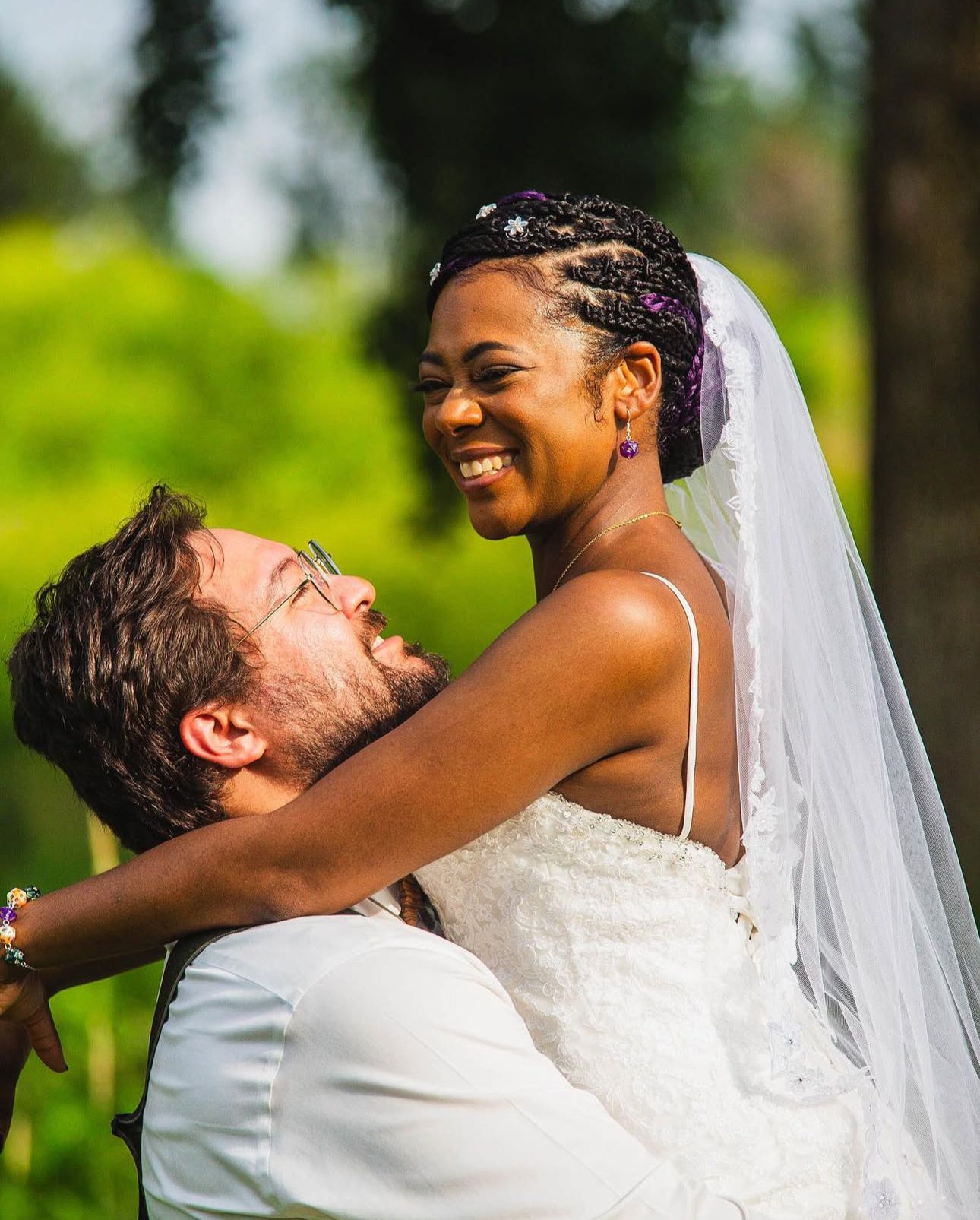 Joyful wedding couple embracing outdoors with bright natural lighting and white bridal gown.