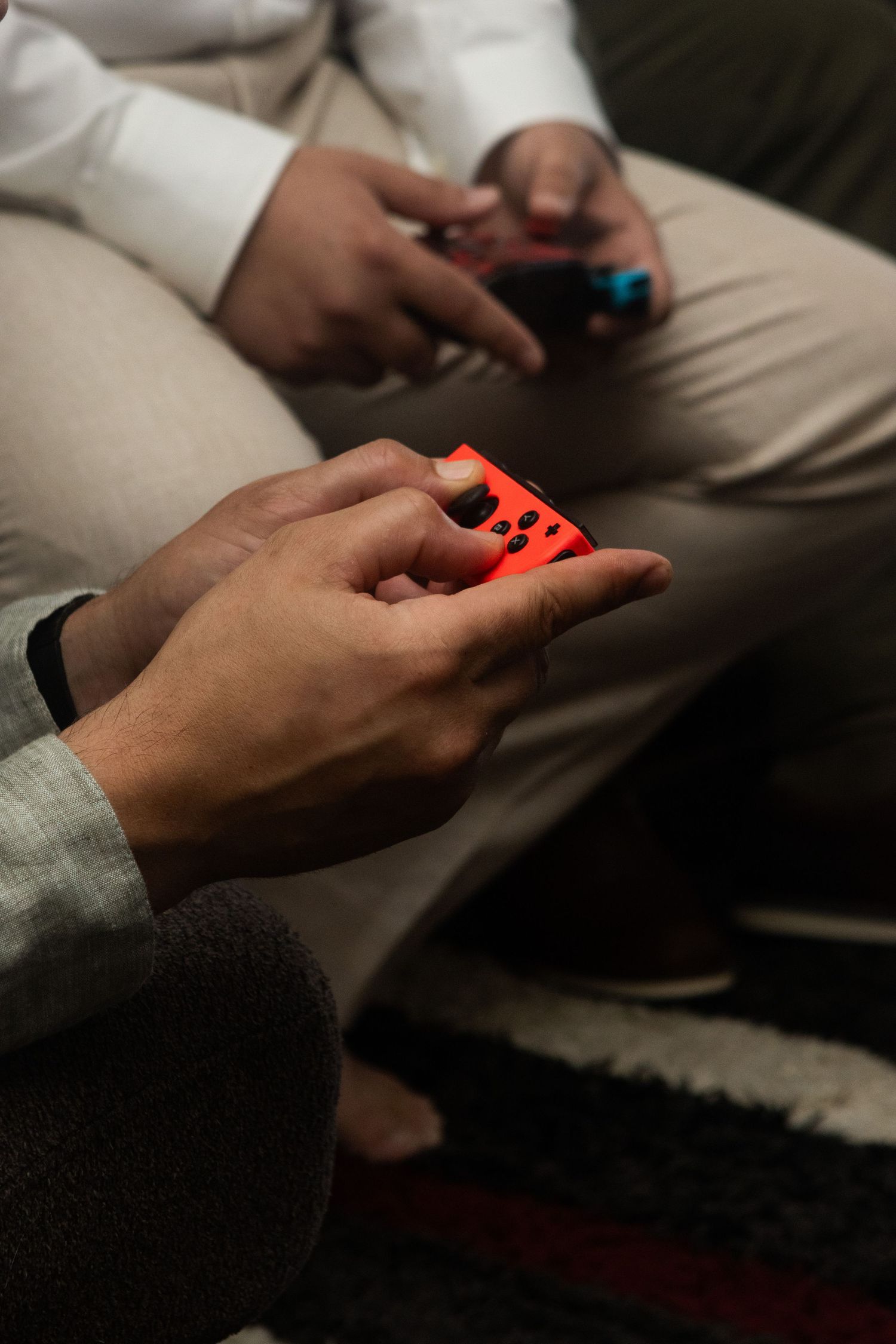 Hands holding red and blue Nintendo Switch Joy-Con controllers while playing video games on a couch.