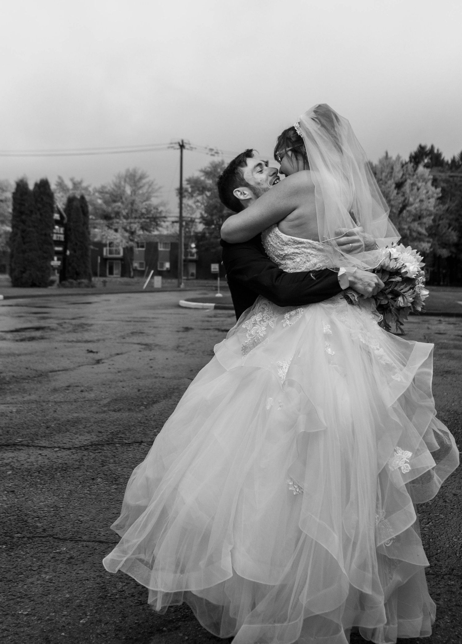 Black and white wedding photo of couple embracing in romantic twirl outdoors.
