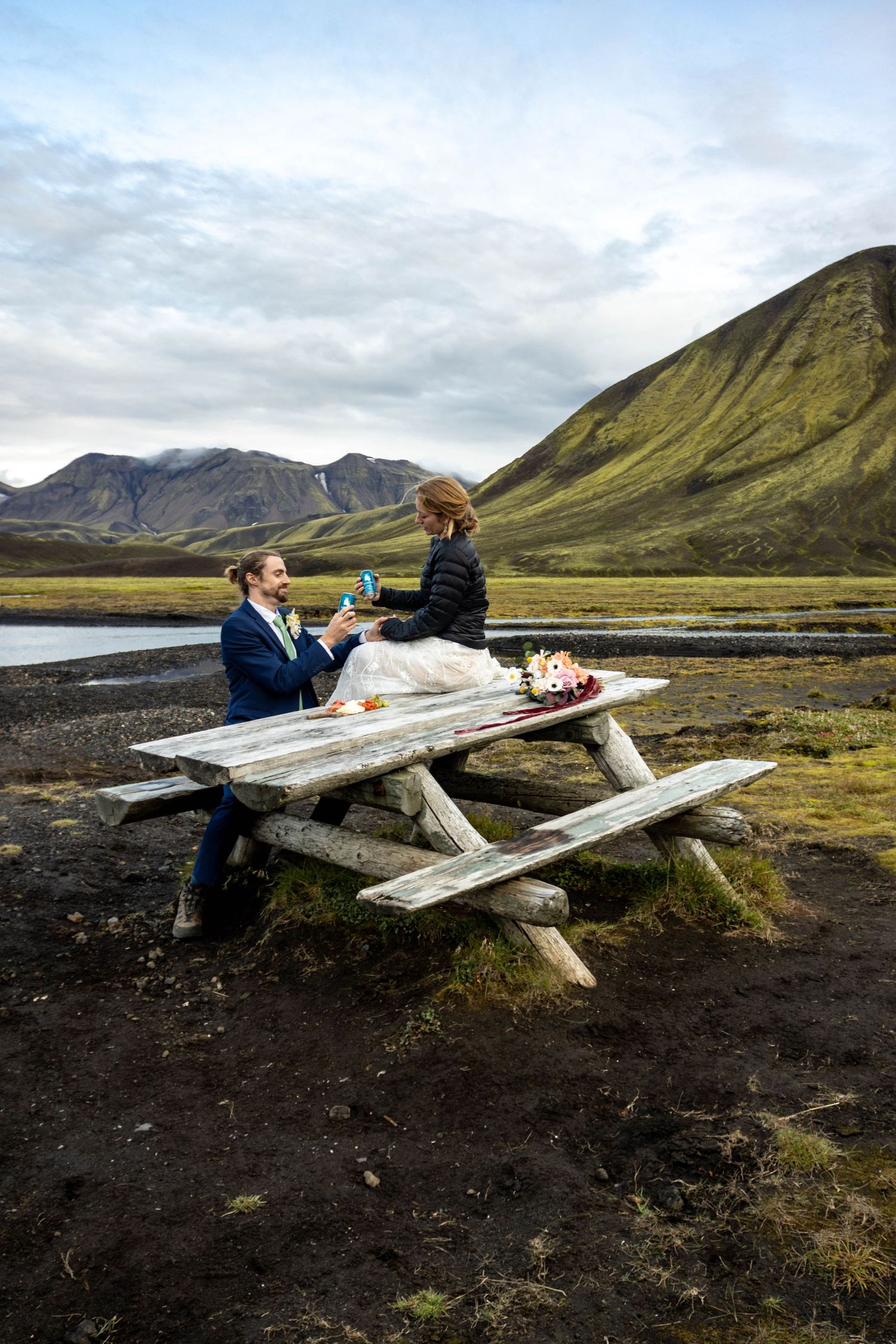 Couple enjoying champagne at picnic table with dramatic mountain landscape in Iceland.