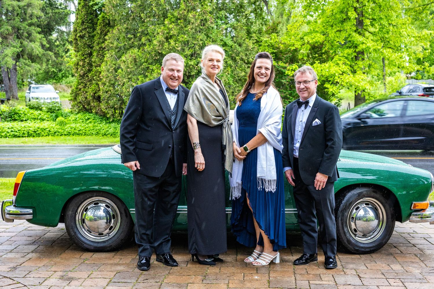 Group poses next to a classic green sports car at an outdoor event.
