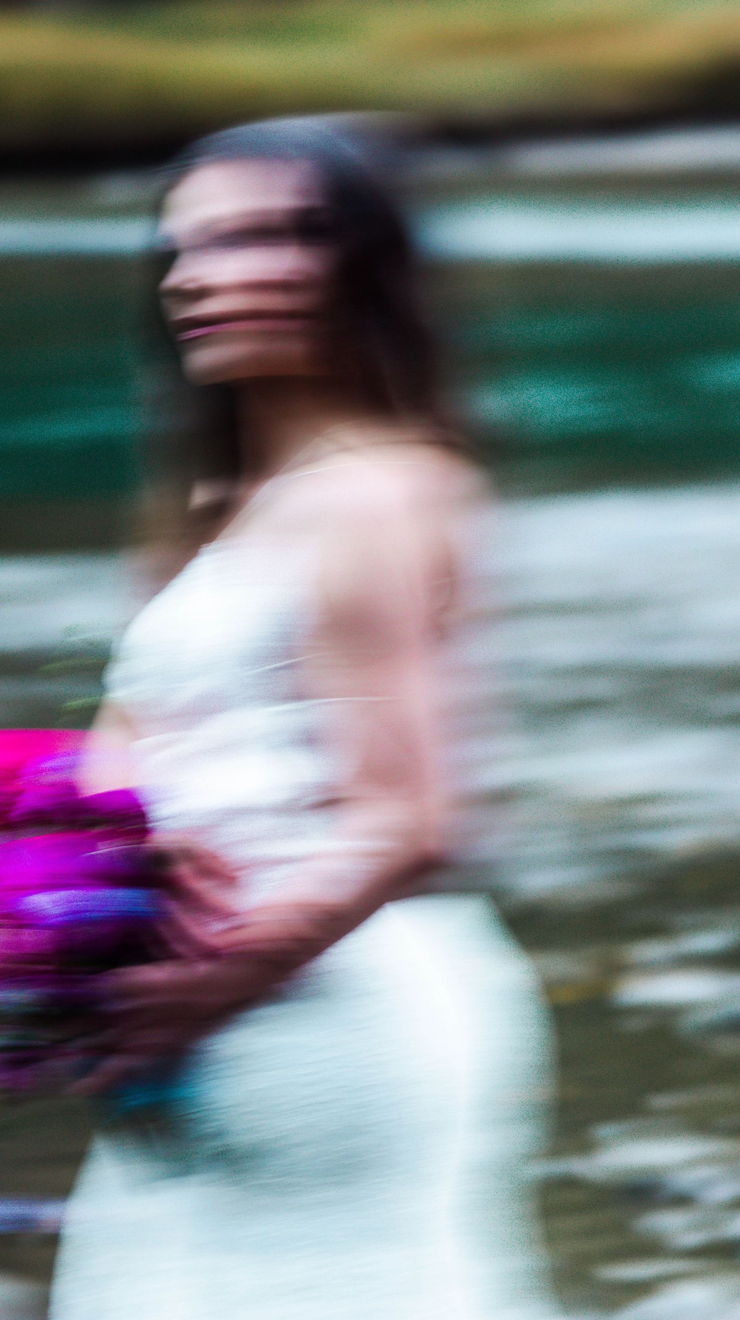 An artistic motion blur portrait of a bride in white holding vibrant purple flowers.