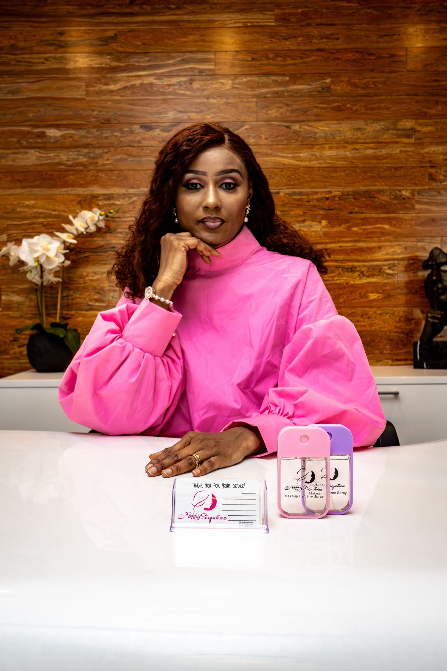 A person in a bright pink sweater poses at a white table with product packaging displayed.