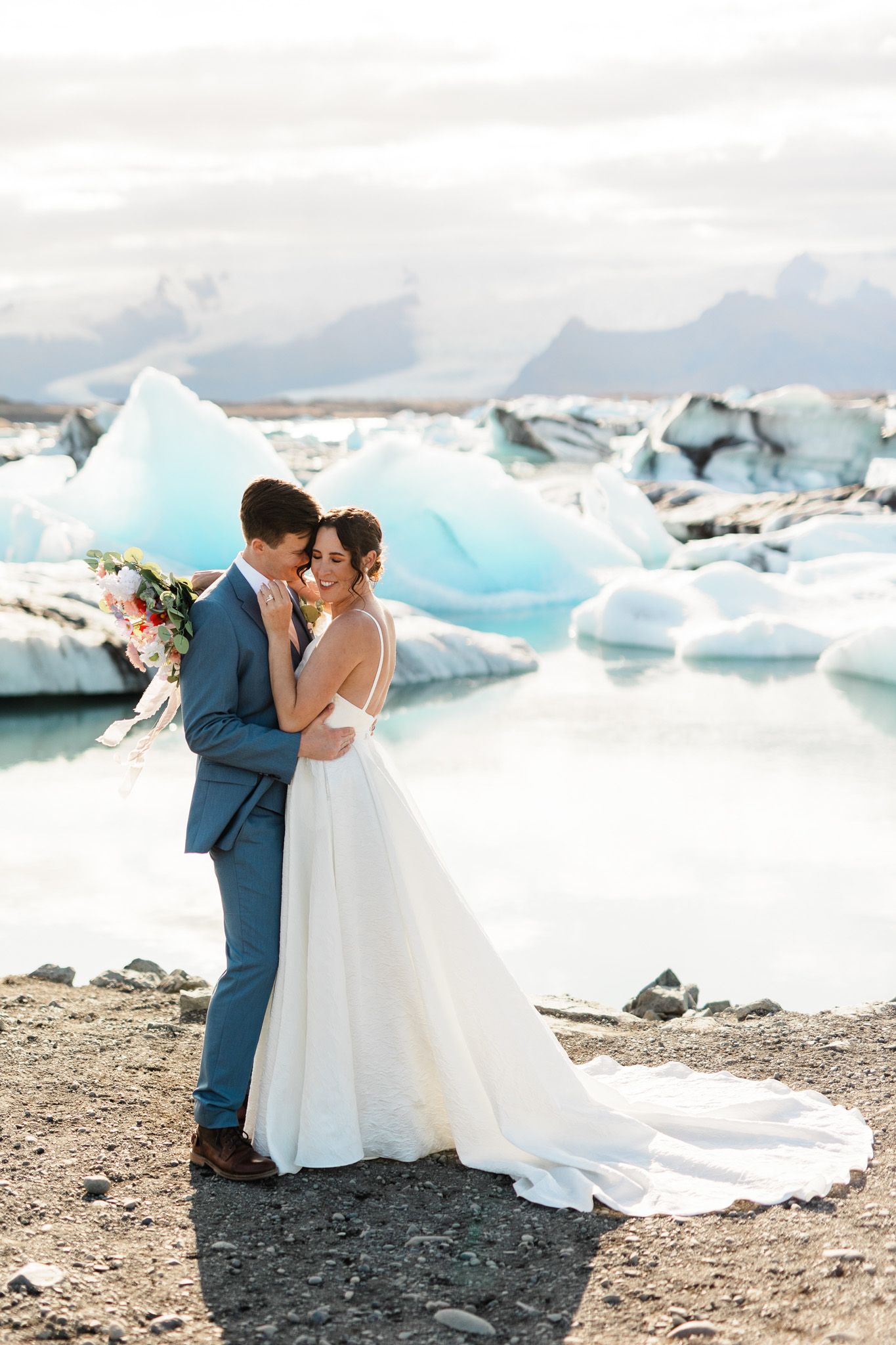 Romantic wedding couple embraces on a black sand beach with stunning blue glacial icebergs in the background.