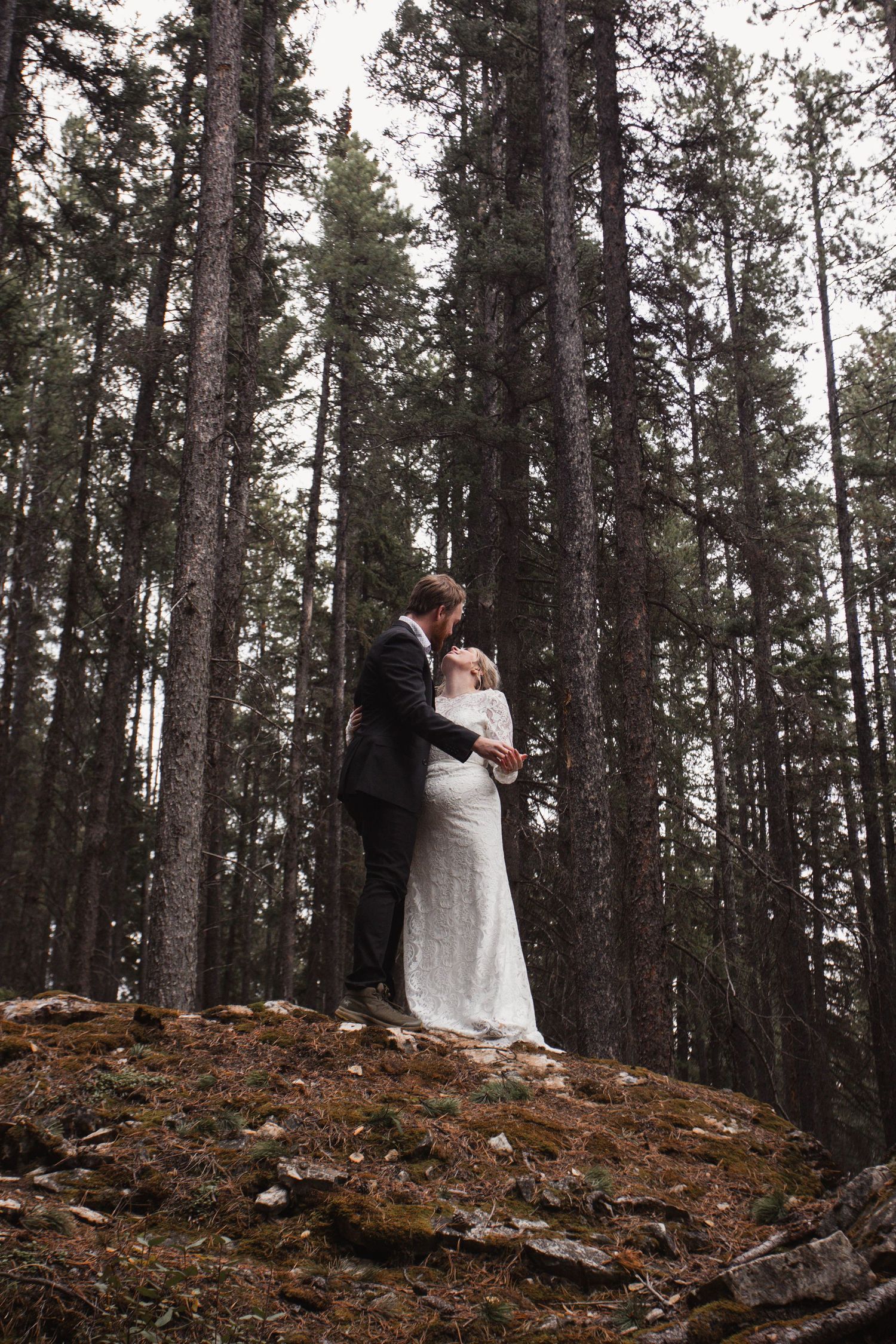 A couple shares an intimate moment on a forest hillside during their wedding photoshoot.