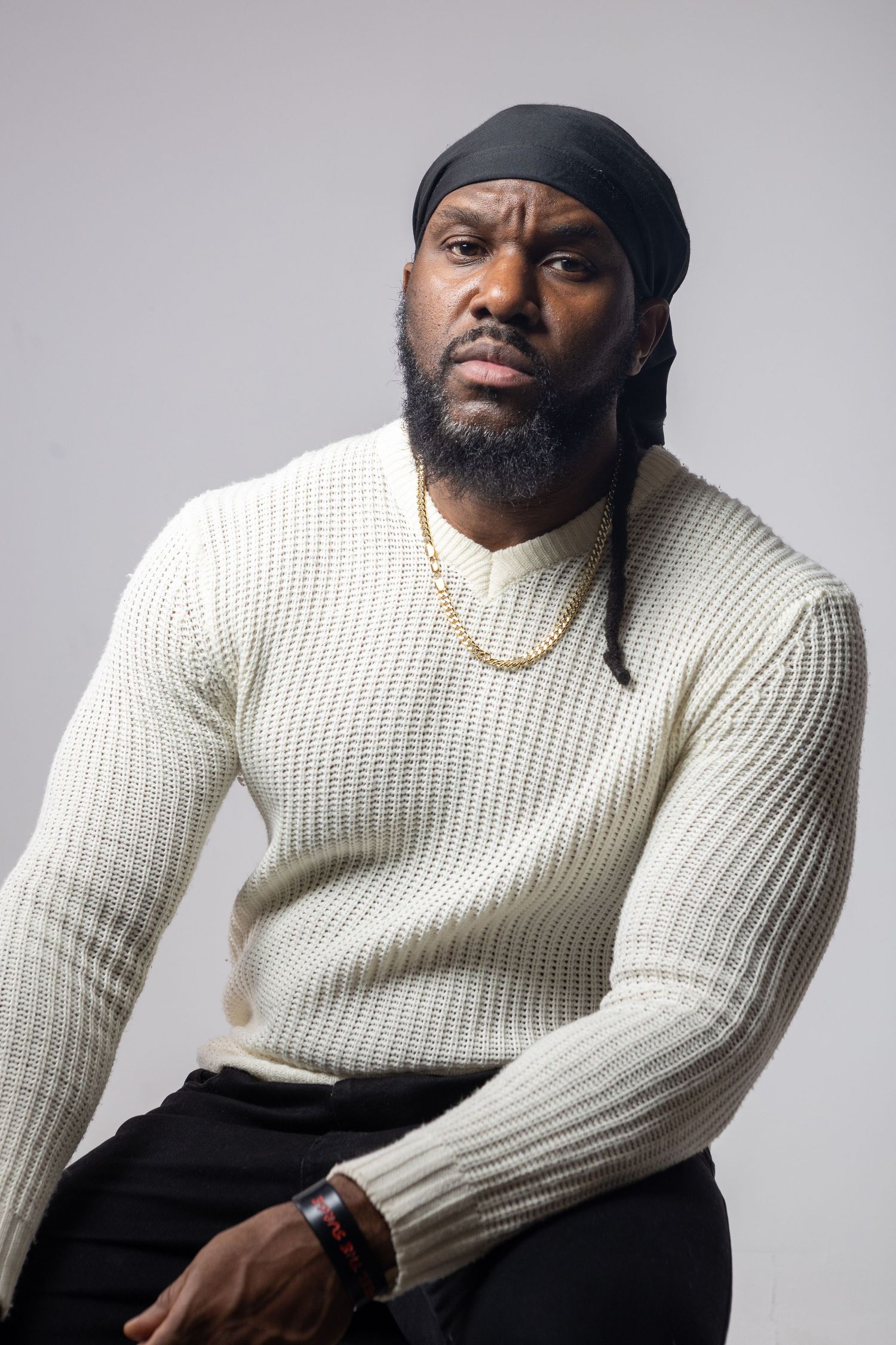 Person wearing a cream knit sweater and black pants poses against a light gray background in a series of artistic portraits.