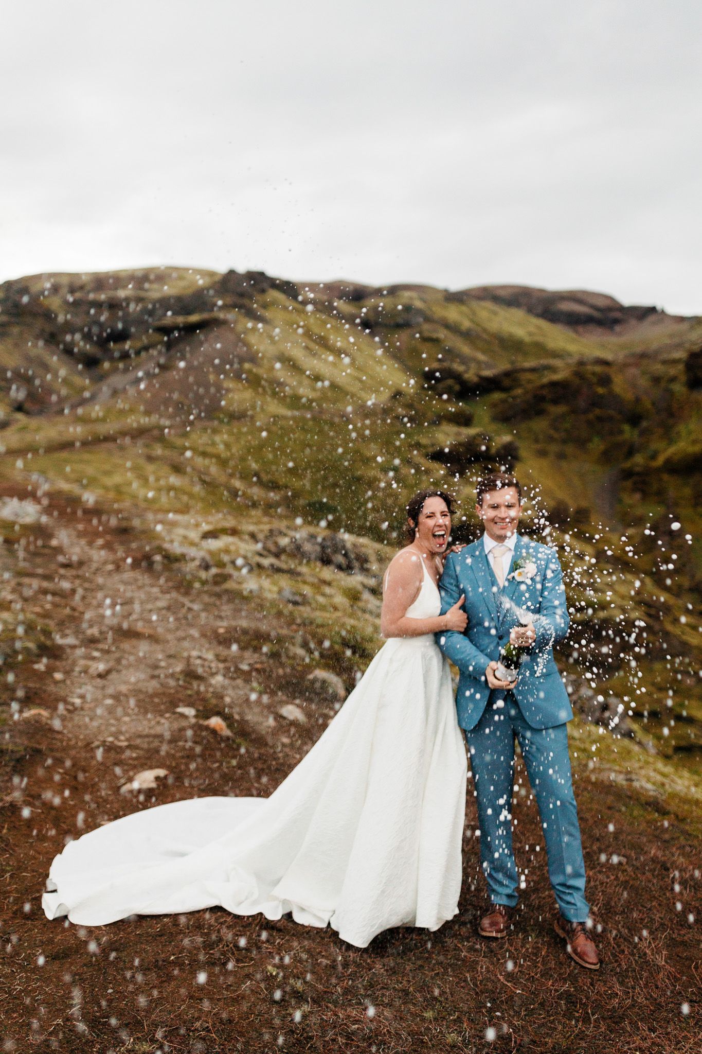 A couple celebrates their wedding day on a scenic mountain trail with confetti falling around them.