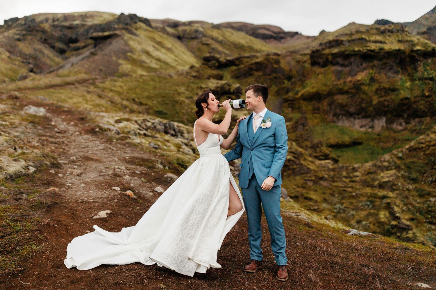 A couple in wedding attire poses in front of dramatic mountainous landscapes in Iceland.