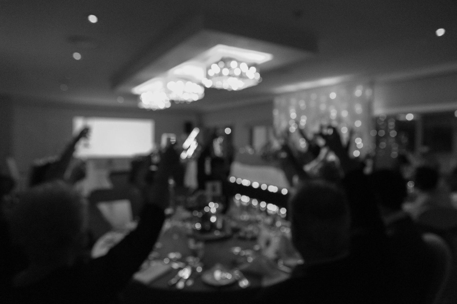Blurred reception party scene with chandelier lighting and celebrating crowd.