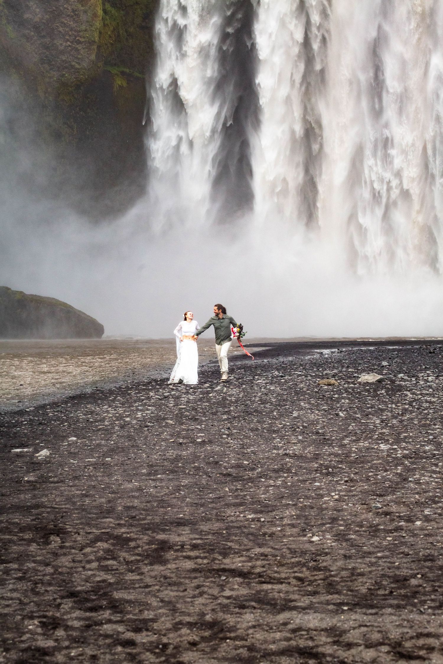 A series of images showing a couple in wedding attire posing near a dramatic misty waterfall on rocky terrain.