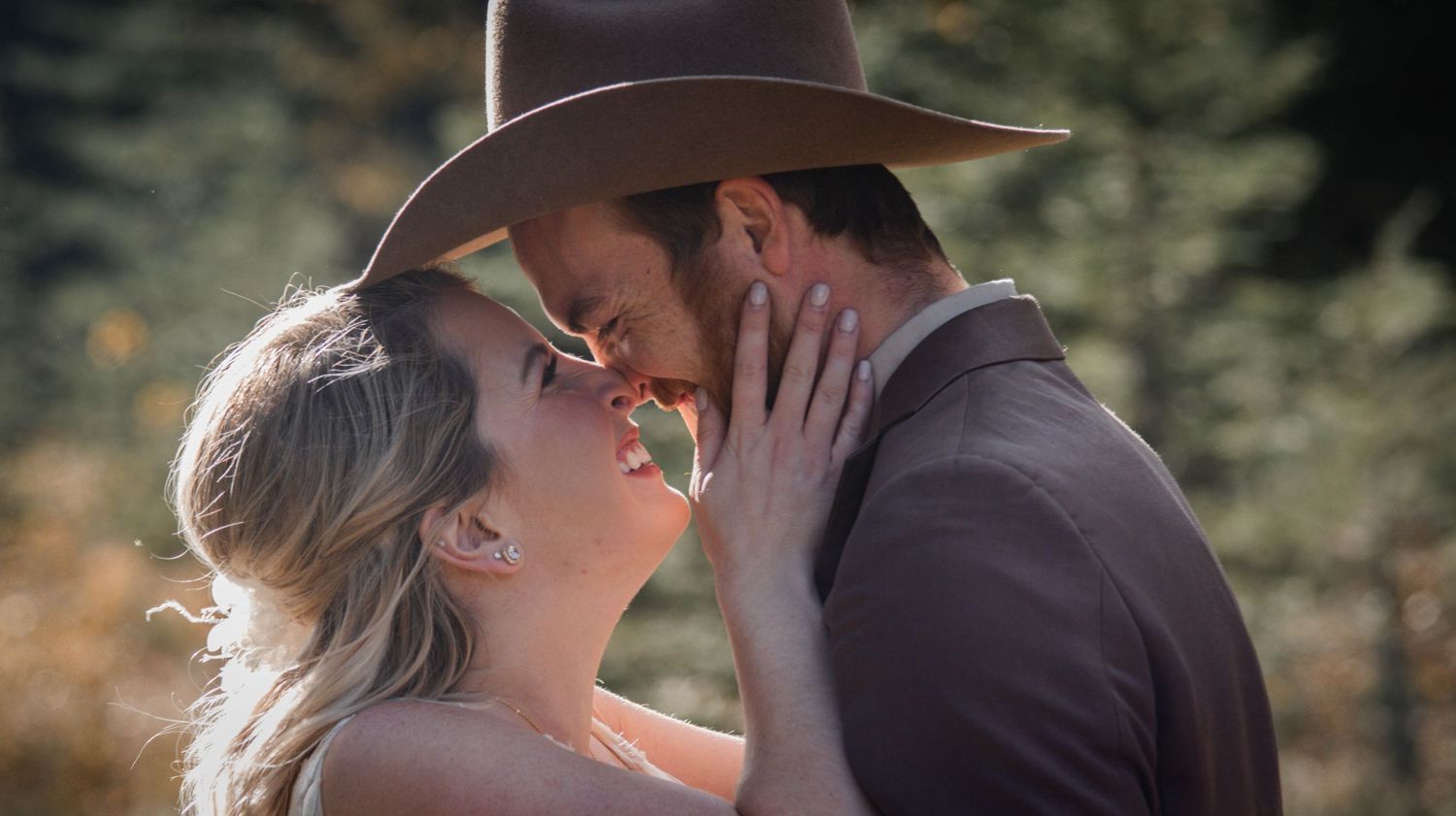 Romantic couple in western attire sharing tender moment in sunlit forest.