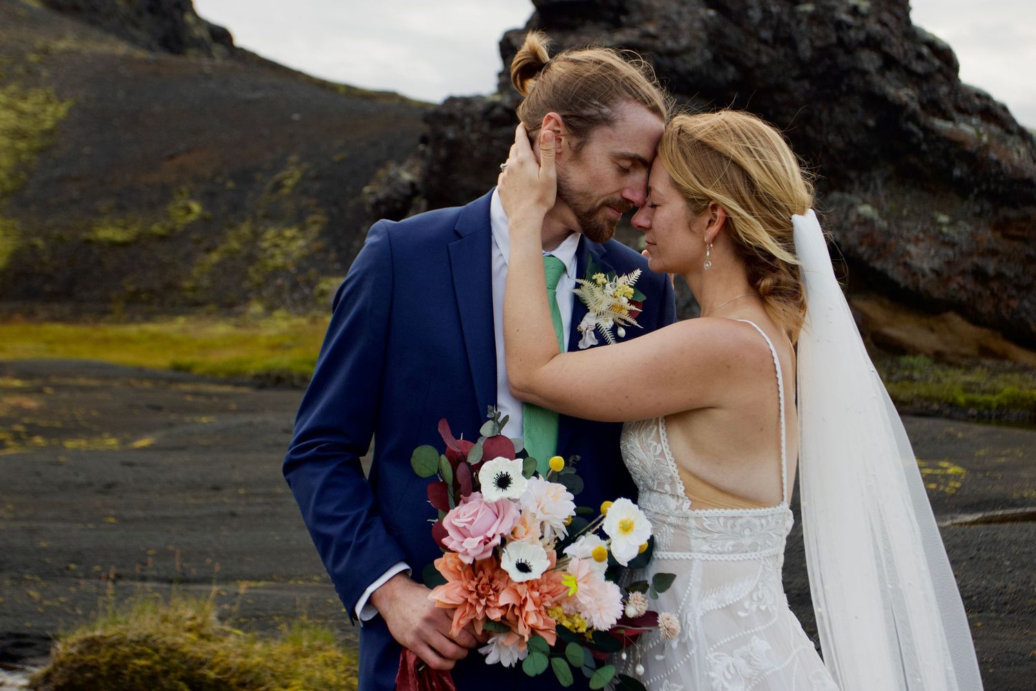 A wedding couple shares romantic moments against dramatic mountain landscapes in Iceland with colorful bouquets.