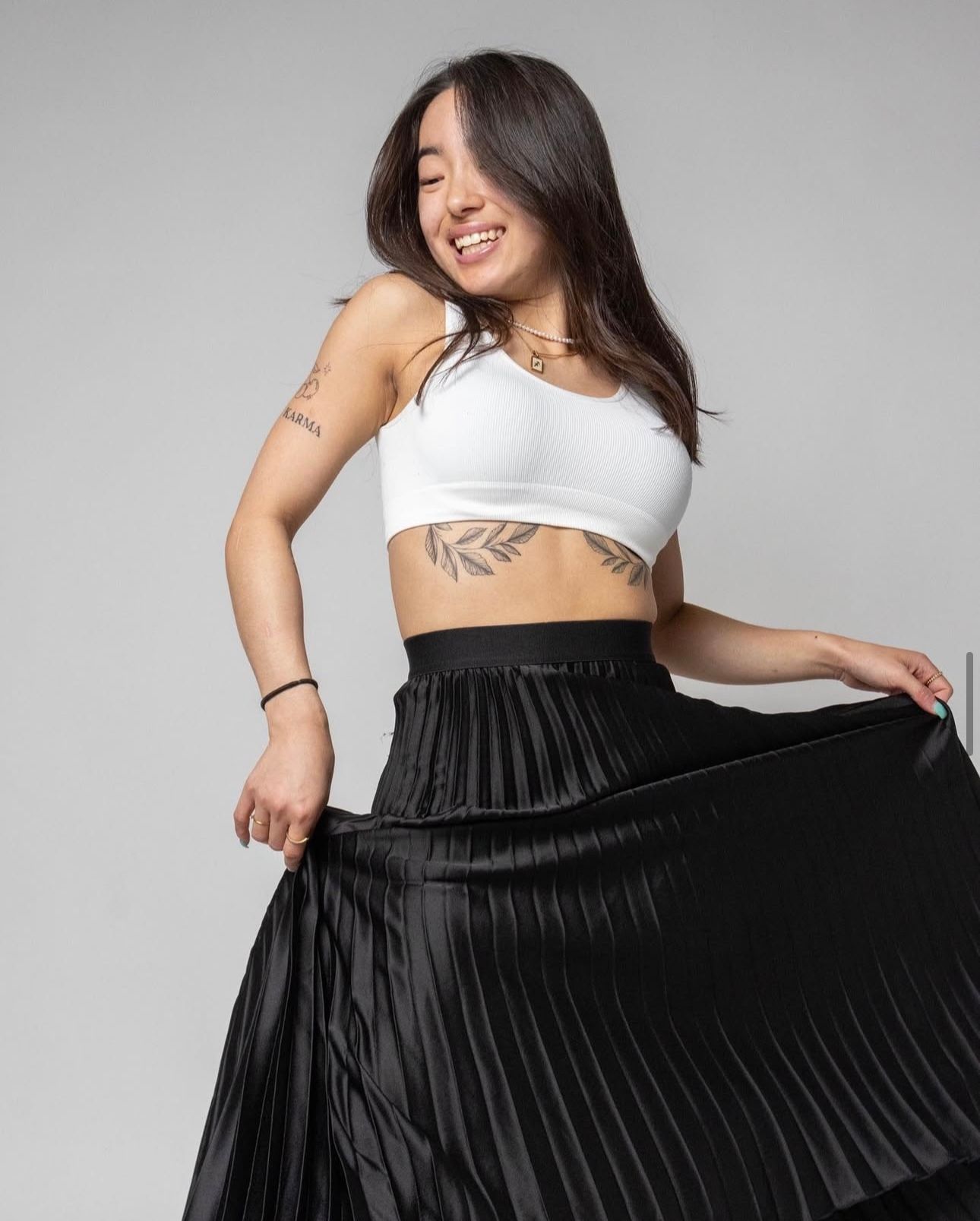 Person in white crop top dancing with flowing black pleated skirt against gray background.