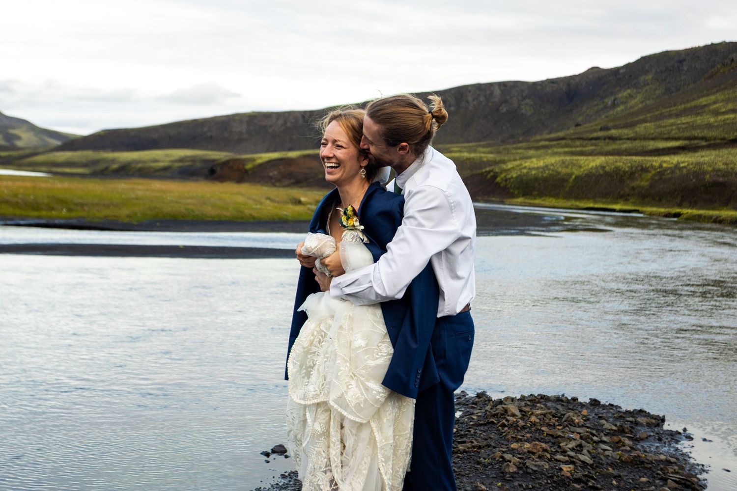 Couple embracing and laughing by a scenic river in Iceland's rugged landscape.