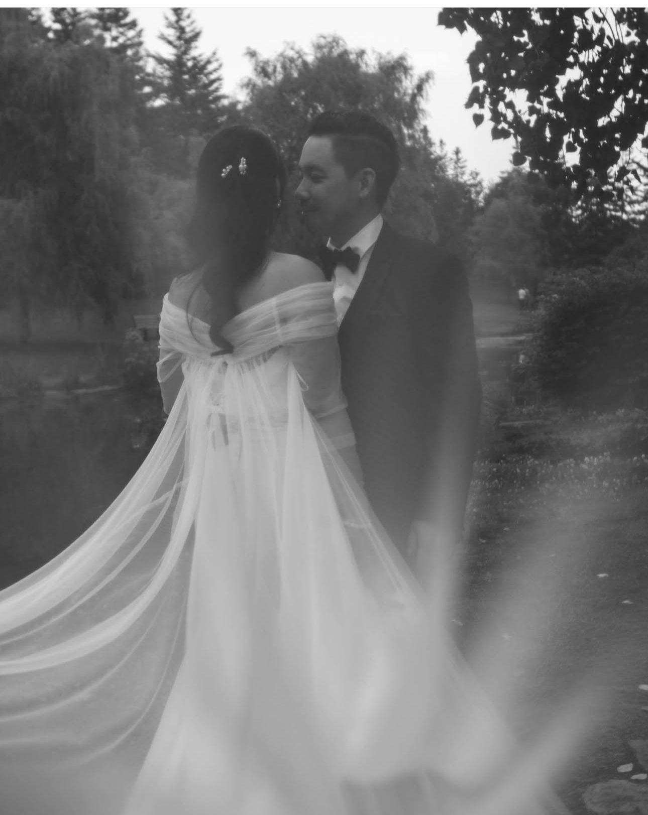 Romantic black and white wedding photo of couple in a dreamy outdoor setting with flowing white dress.