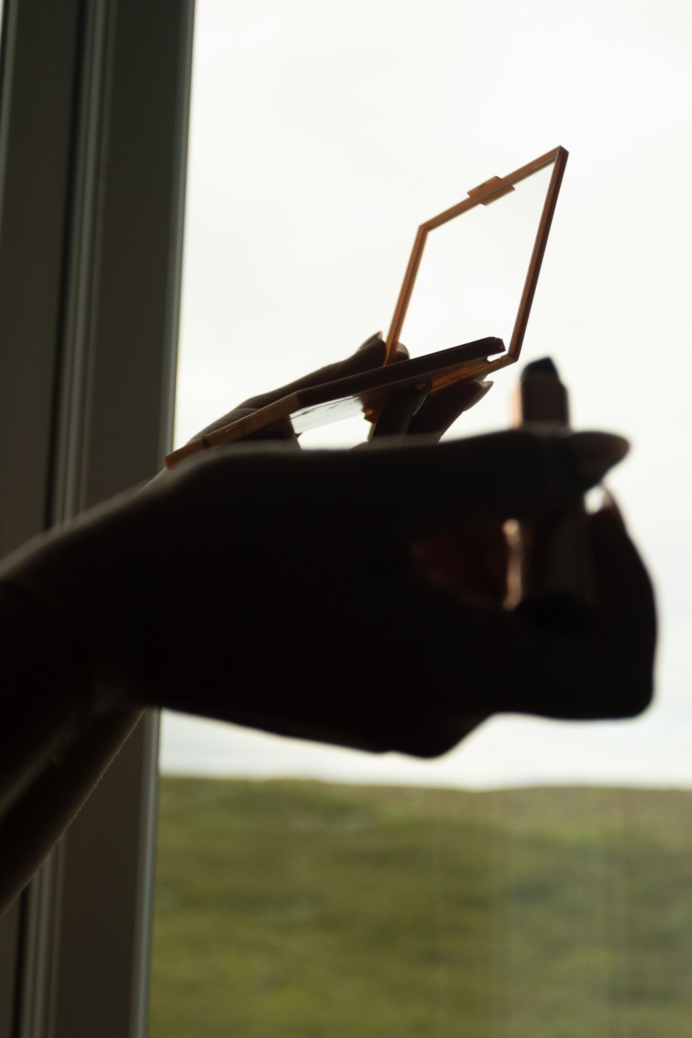Silhouette of hand holding picture frame against window with countryside view.