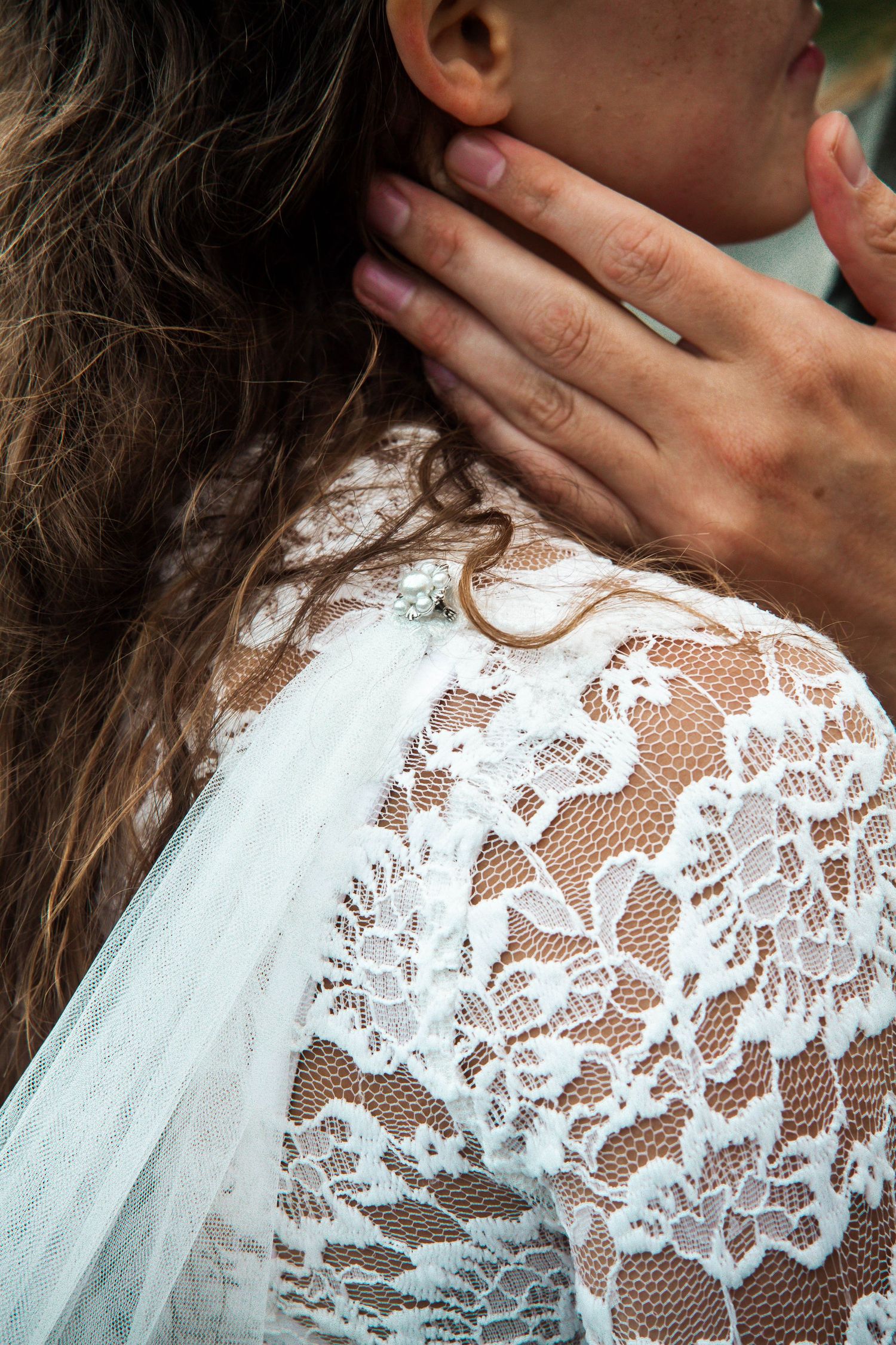 Close-up detail of delicate white lace pattern on a wedding dress shoulder against a dark background.