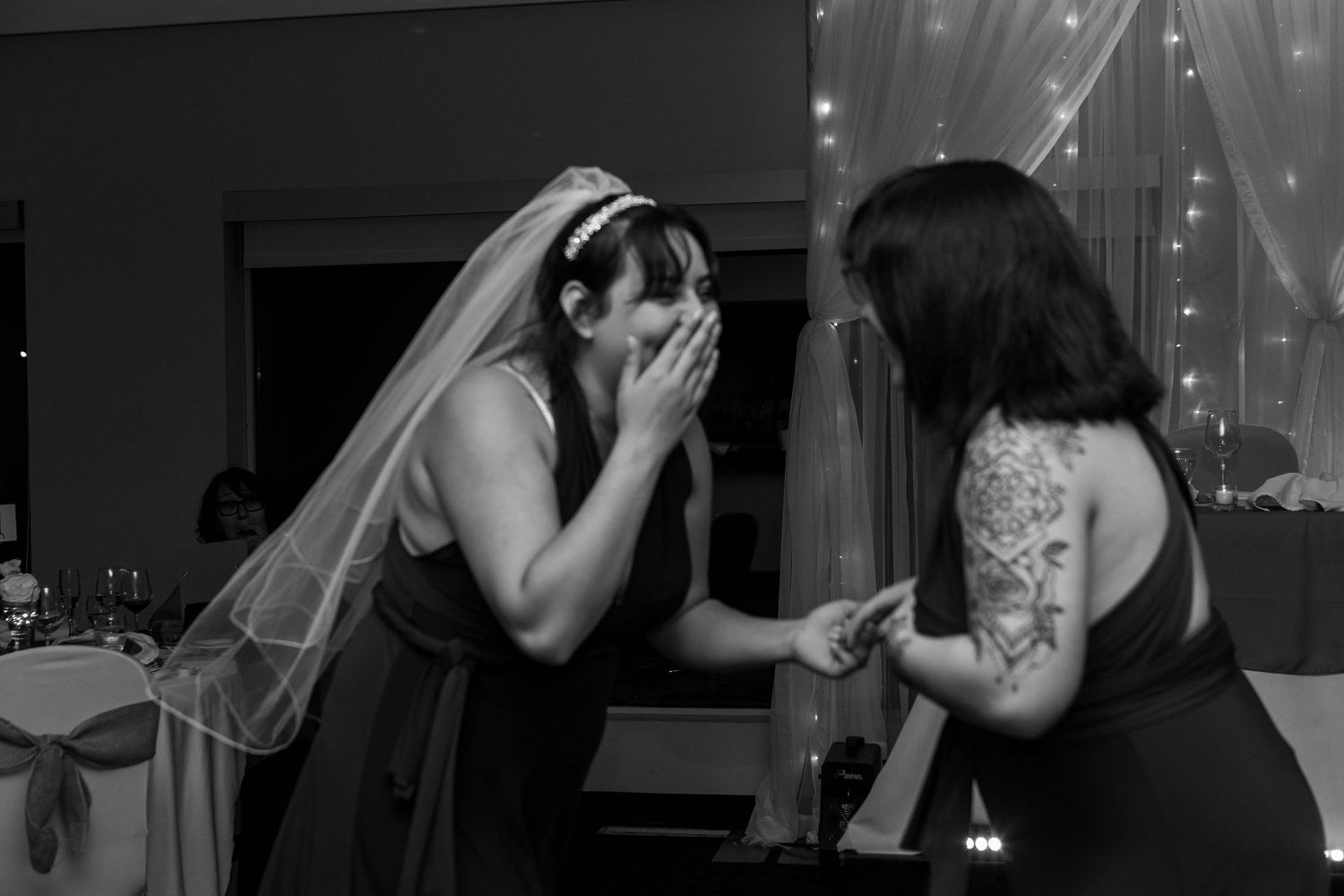 An emotional moment between a bride in a veil and another person during a wedding celebration with string lights in background.