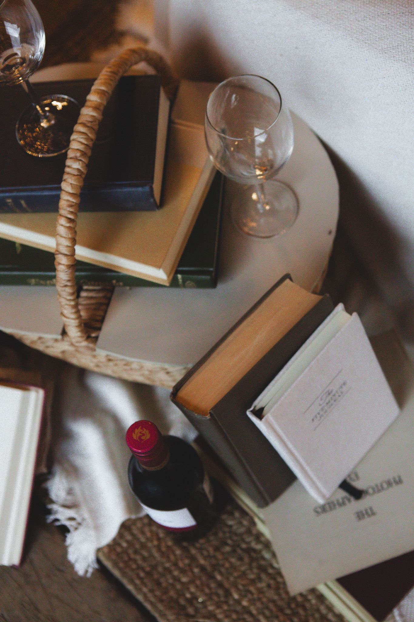 Cozy still life with books, wine glass, and woven basket on wooden surface.
