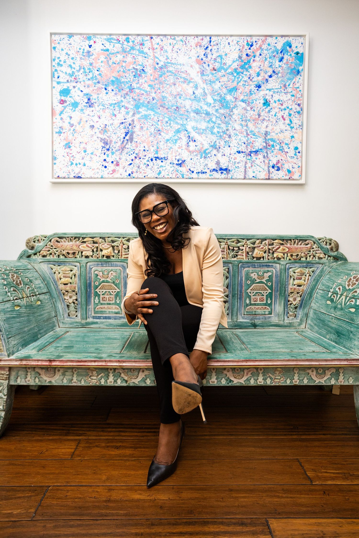 A vintage turquoise bench sits against a white wall with abstract blue and pink artwork displayed above.