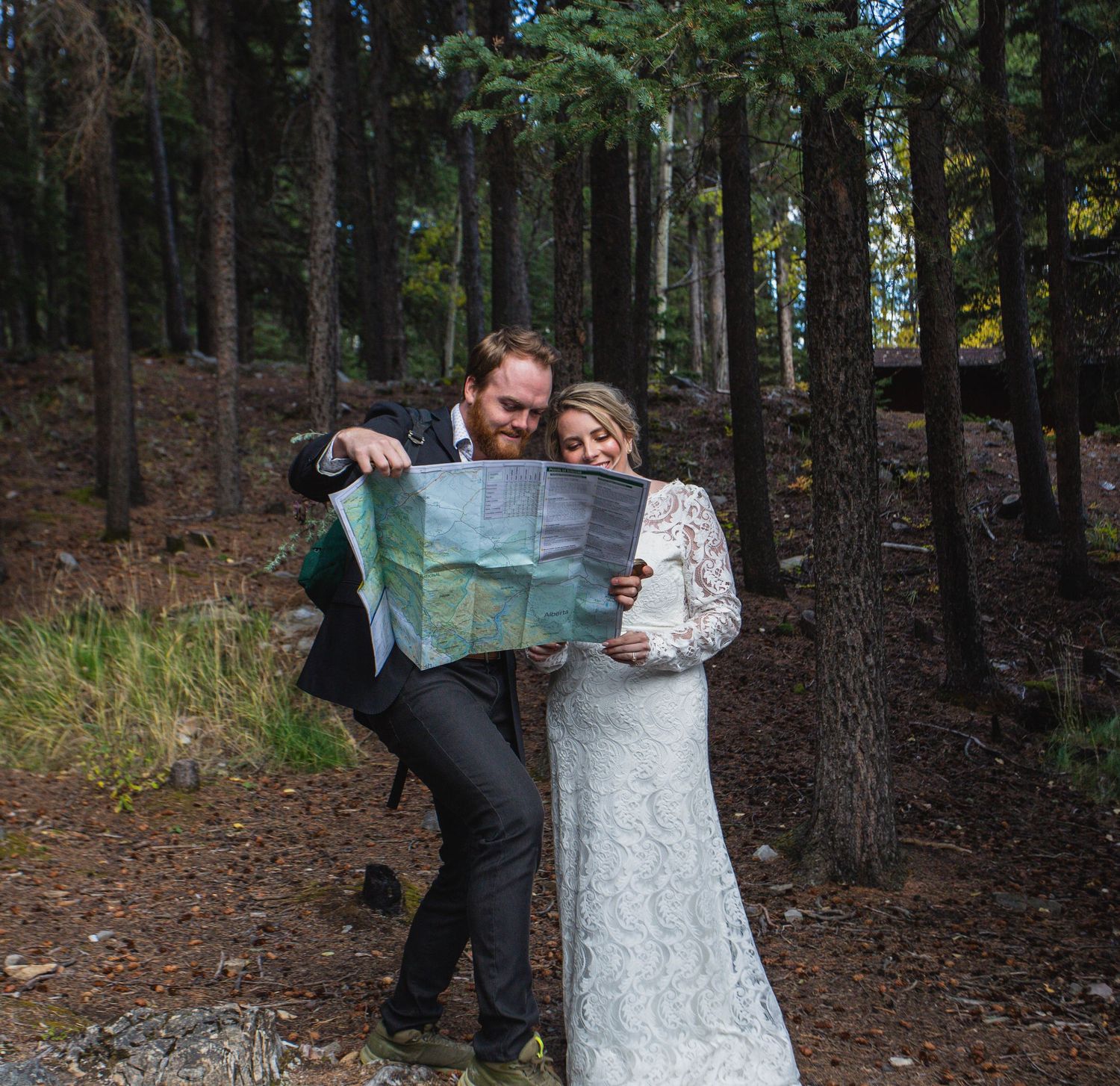 Two people look at a map together while standing in a wooded forest area.